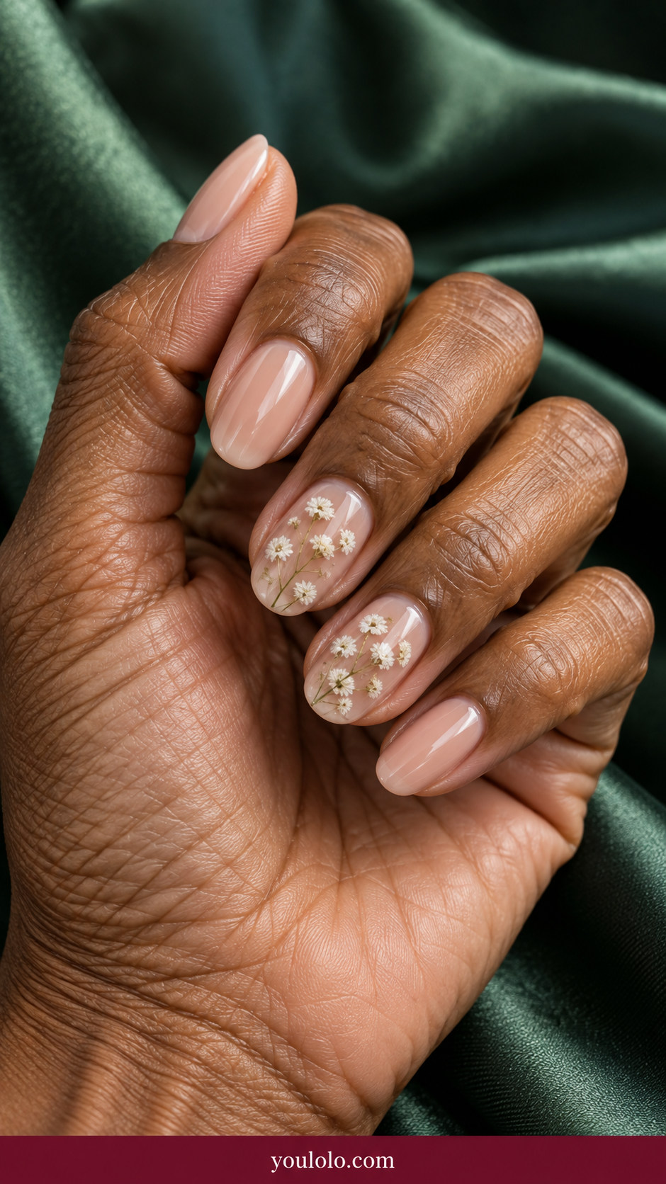Pressed Flower Nails idea 1: tiny flat dried white baby's-breath flowers encapsulated under transparent gel on two nude nails on an anatomically realistic feminine hand