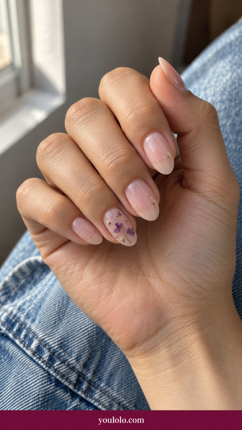 Pressed Flower Nails idea 2: delicate dried violet petals under clear gel on one sheer pink accent nail on an anatomically realistic feminine hand