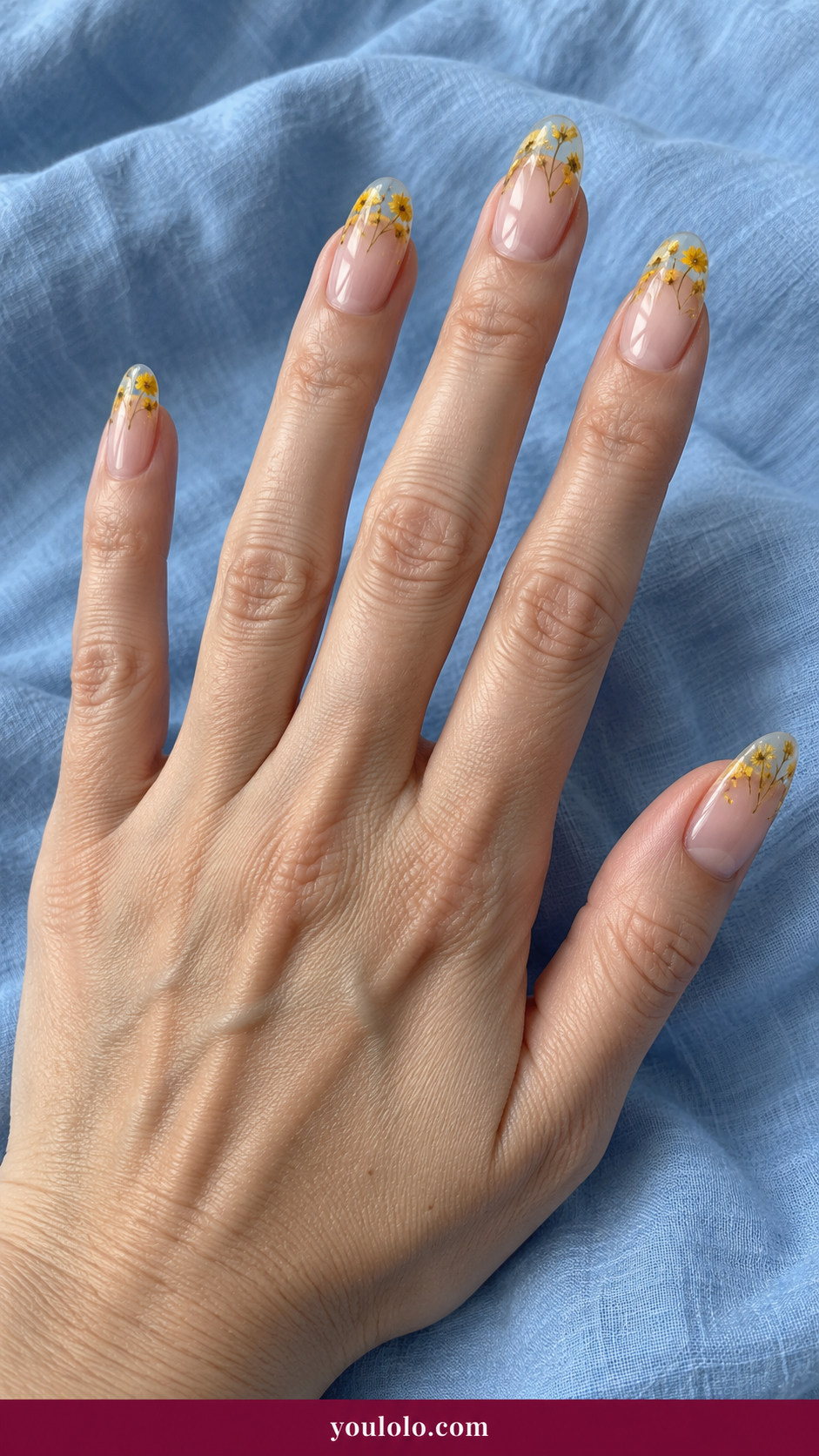 Pressed Flower Nails idea 4: miniature dried yellow blossoms sealed within translucent nude gel French tips on an anatomically realistic feminine hand