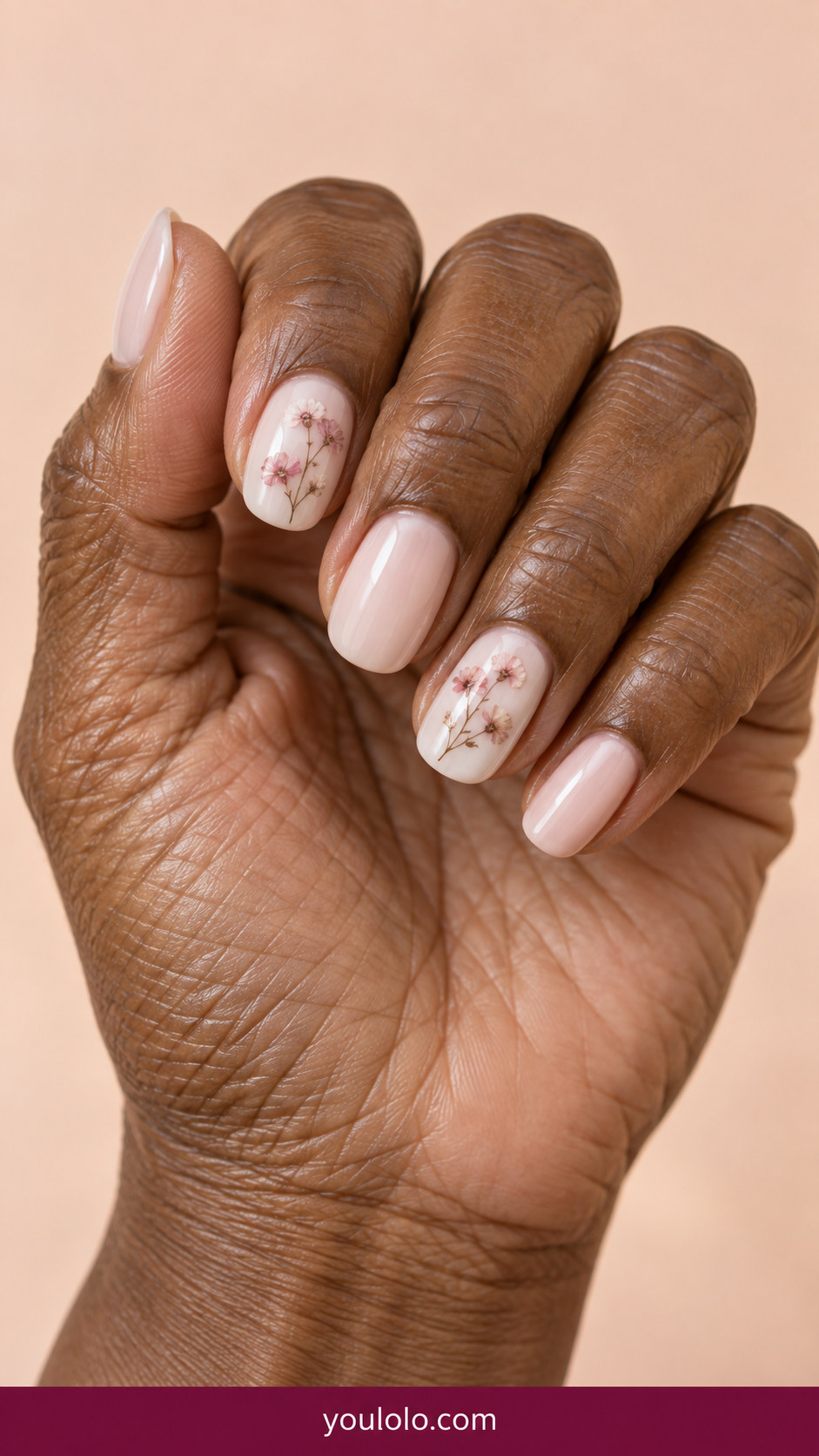 Pressed Flower Nails idea 6: tiny muted pink pressed flowers over milky-white polish on two nails on an anatomically realistic feminine hand