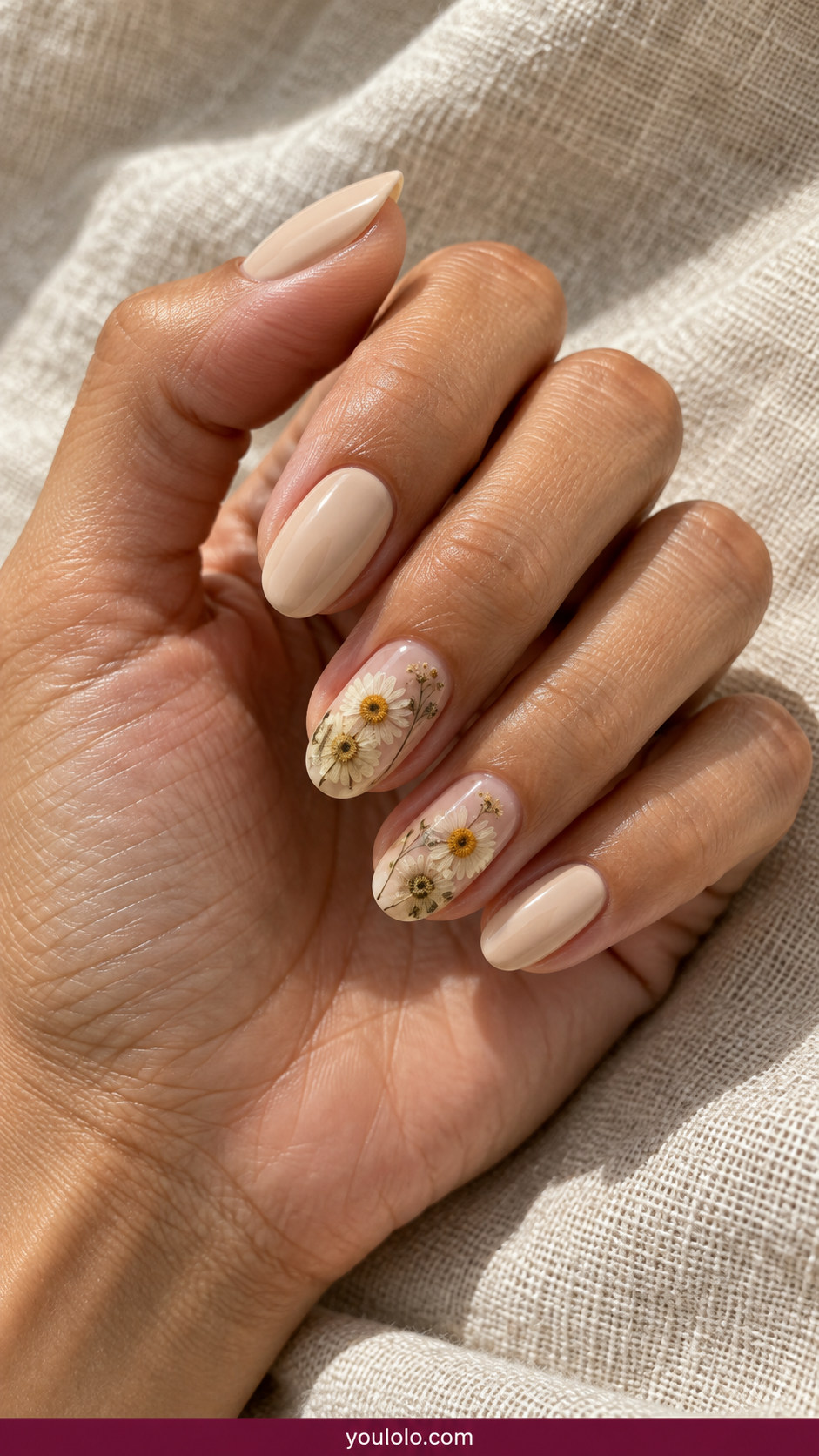 Pressed Flower Nails idea 9: small pressed chamomile blossoms under clear gel beside pale beige solids on an anatomically realistic feminine hand