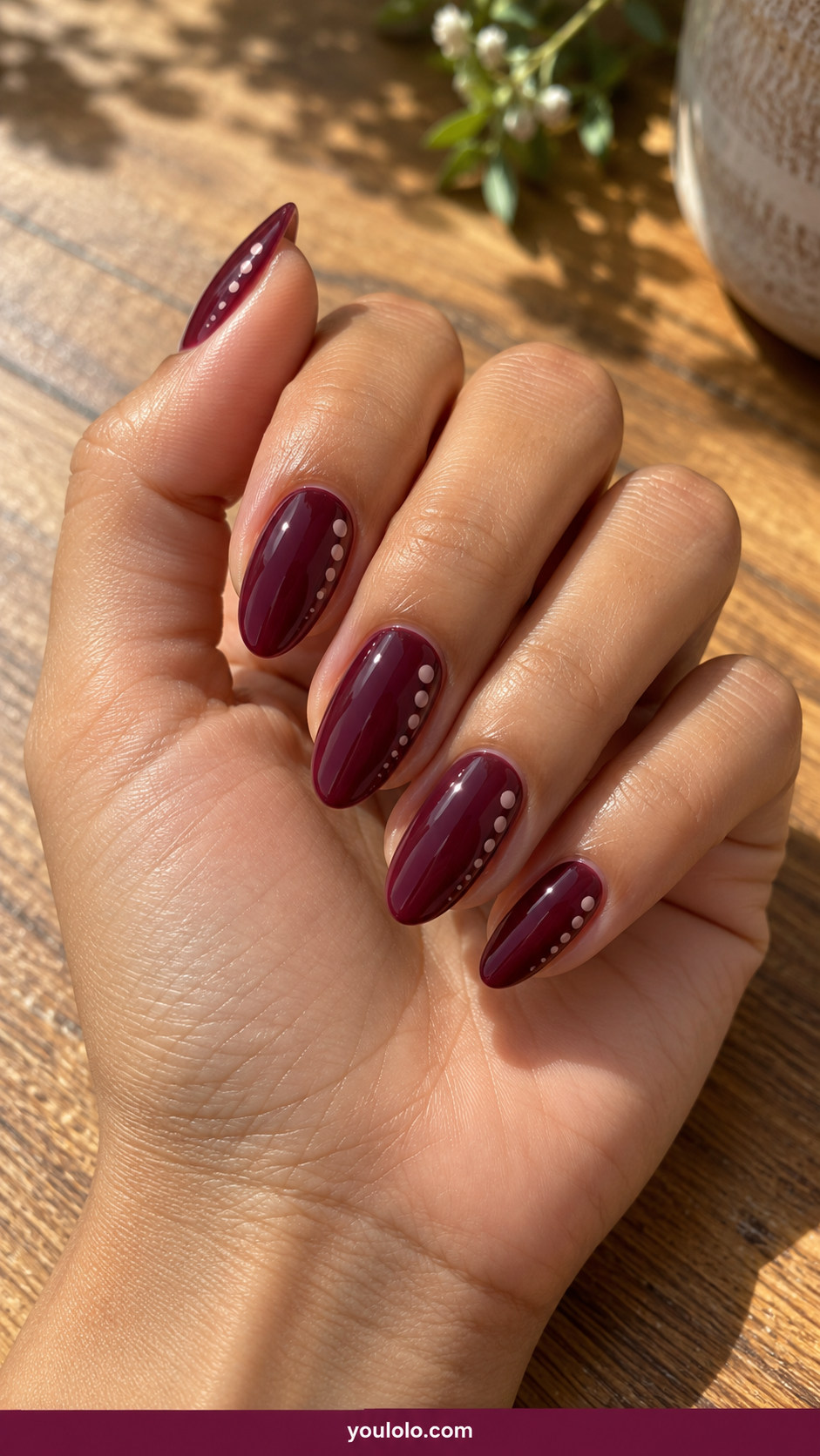 Polka Dot Nails idea 12: burgundy almond nails with restrained tiny pale blush dots along one edge on an anatomically realistic feminine hand