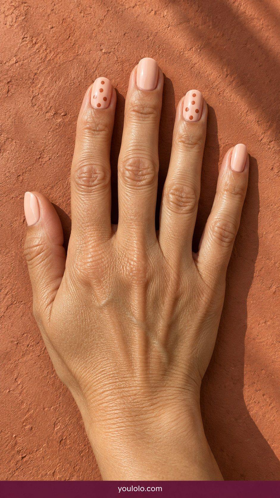 Polka Dot Nails idea 13: pale peach nails with staggered terracotta dot rows on two fingers on an anatomically realistic feminine hand
