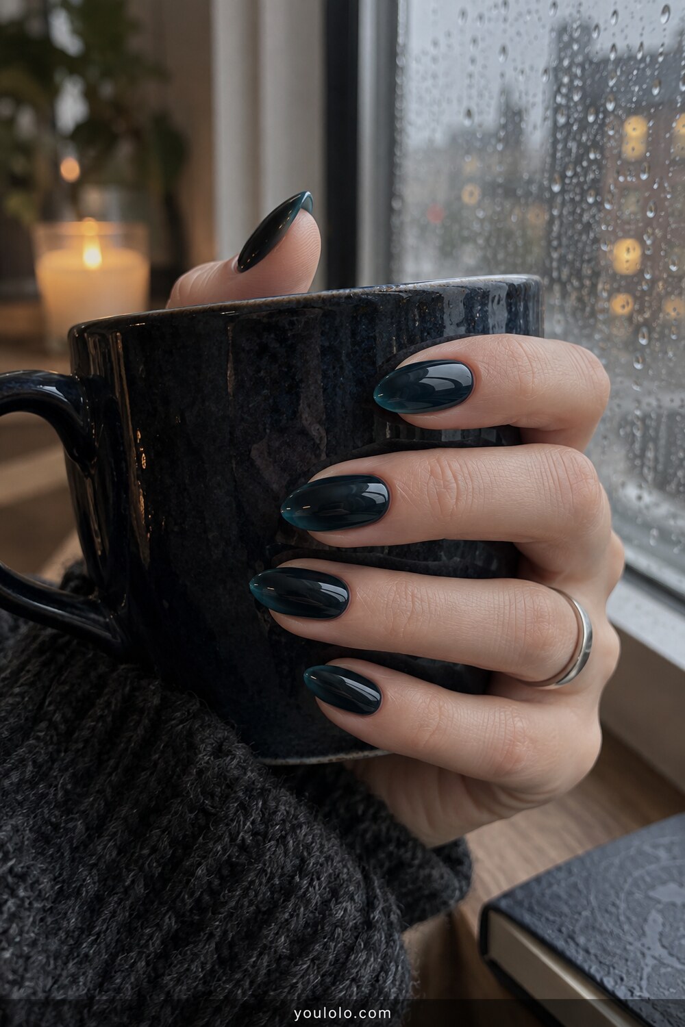 Blackened teal glass almond nails beside a rainy window
