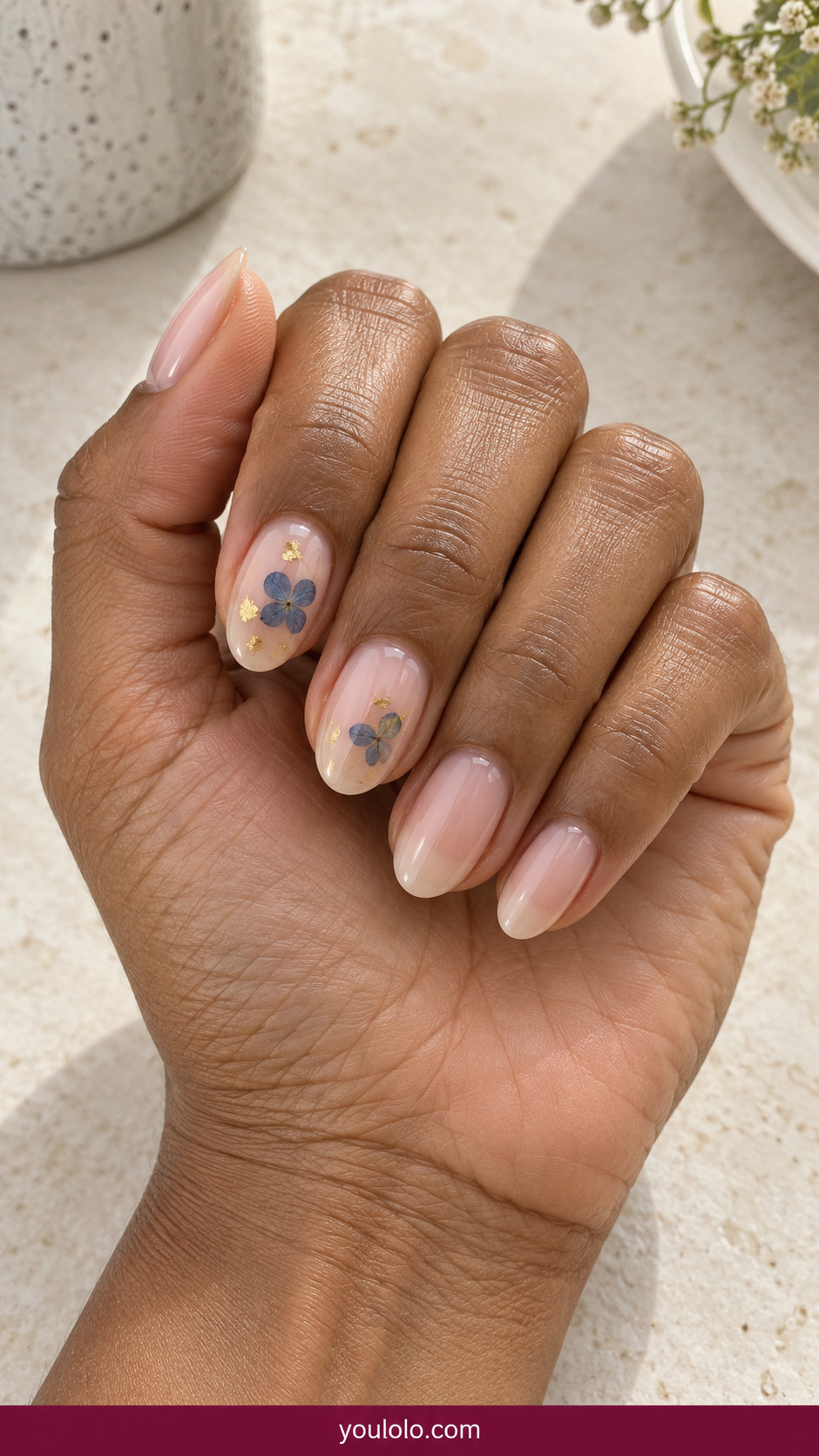Pressed Flower Nails idea 14: one pressed blue petal and a tiny gold foil fleck on clear accent nails on an anatomically realistic feminine hand