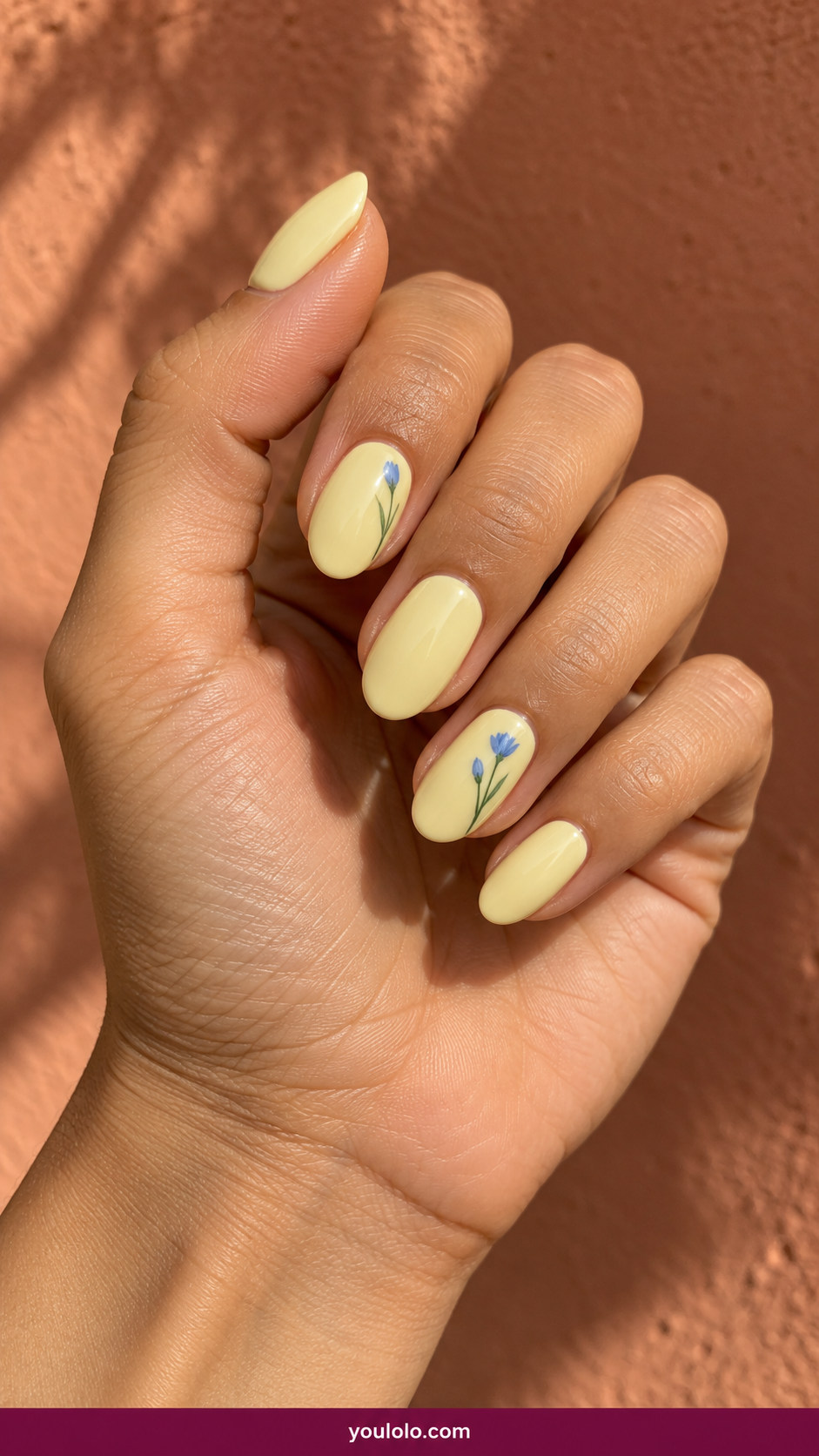 Butter Yellow Nails idea 14: pale lemon-butter nails with two tiny cornflower-blue floral buds on an anatomically realistic feminine hand