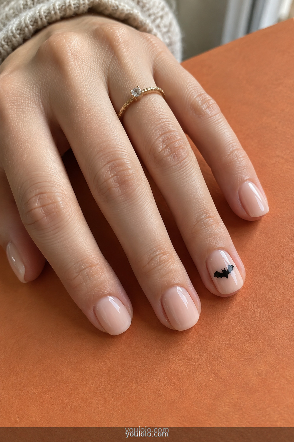 Nude short nails with one tiny black bat sticker accent