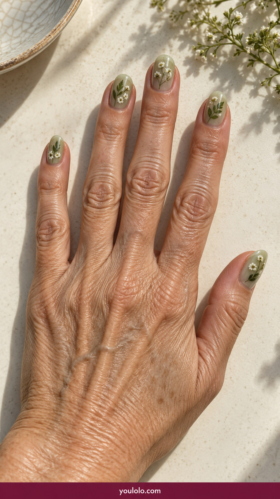 Pressed Flower Nails idea 17: botanical pressed leaf and tiny white blossom sealed in pale sage gel on an anatomically realistic feminine hand