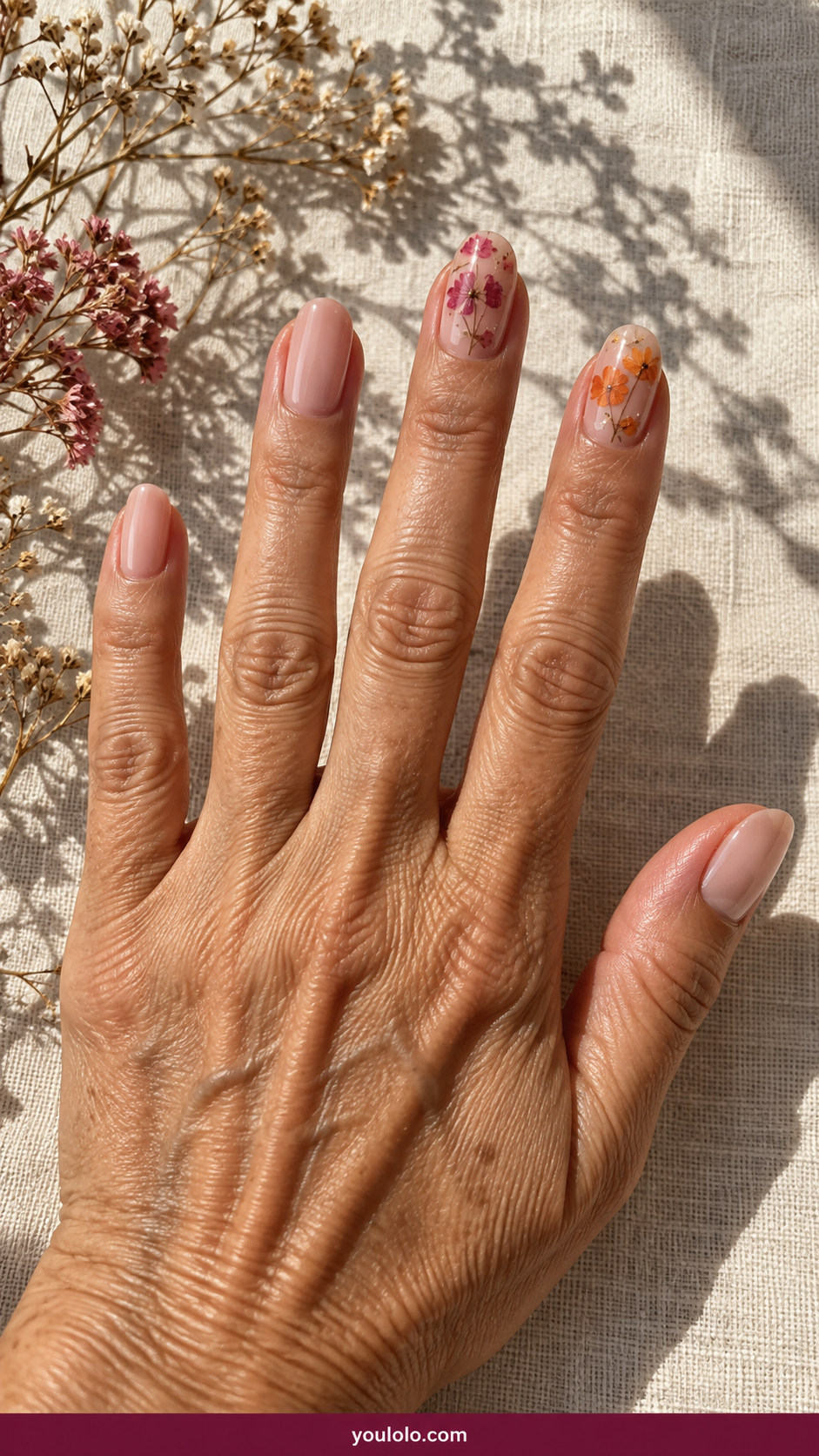 Pressed Flower Nails idea 20: mixed pressed pink and orange tiny dried blossoms under smooth clear gel on two accents on an anatomically realistic feminine hand