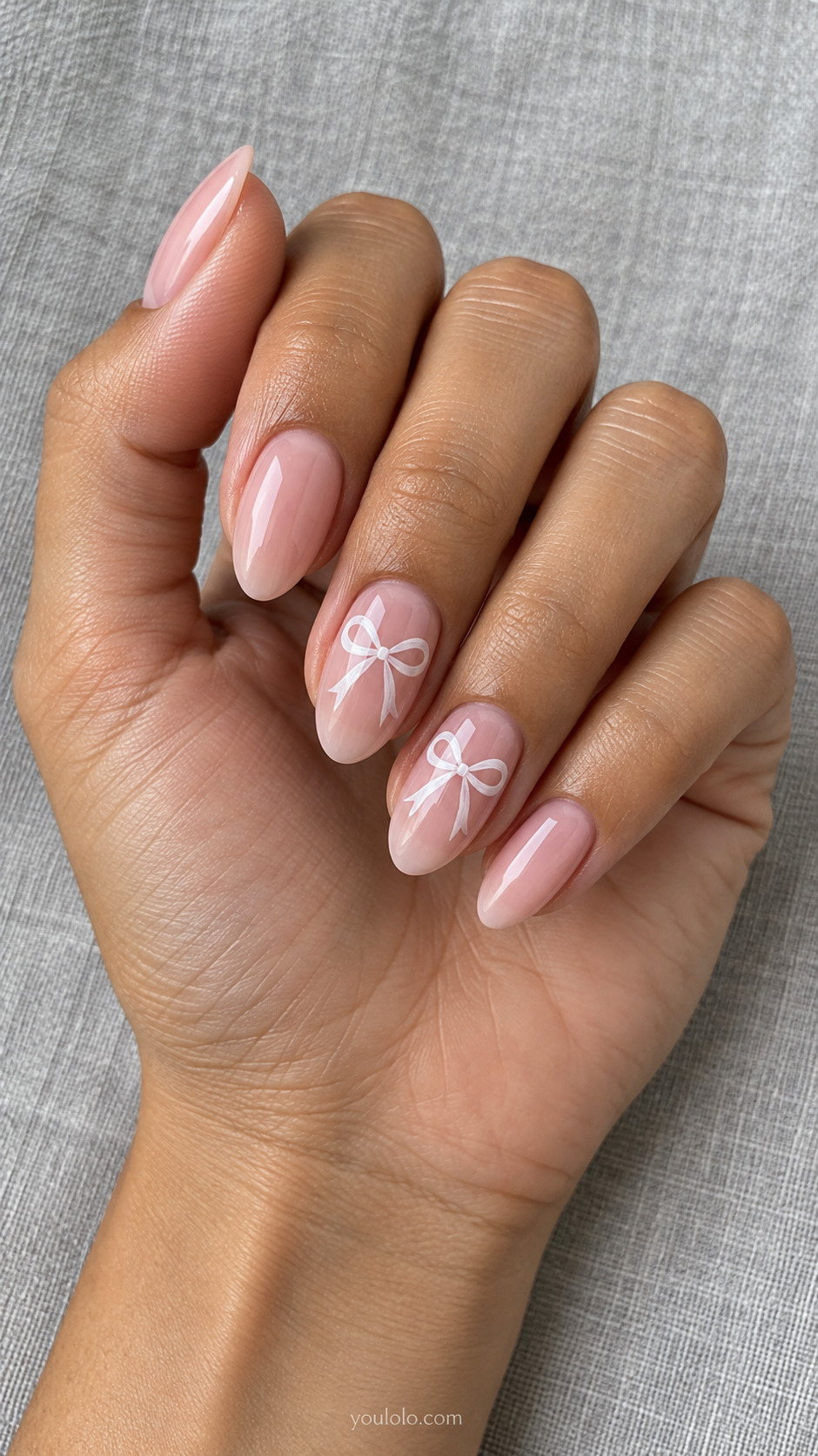Almond blush pink nails with white painted ribbon bows on two accent nails