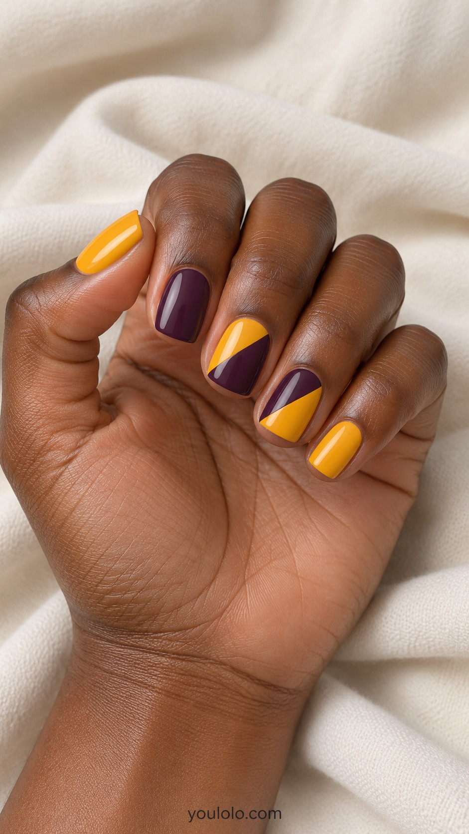 Short squoval nails alternating saffron yellow and aubergine with clean diagonal two tone blocks on middle and ring