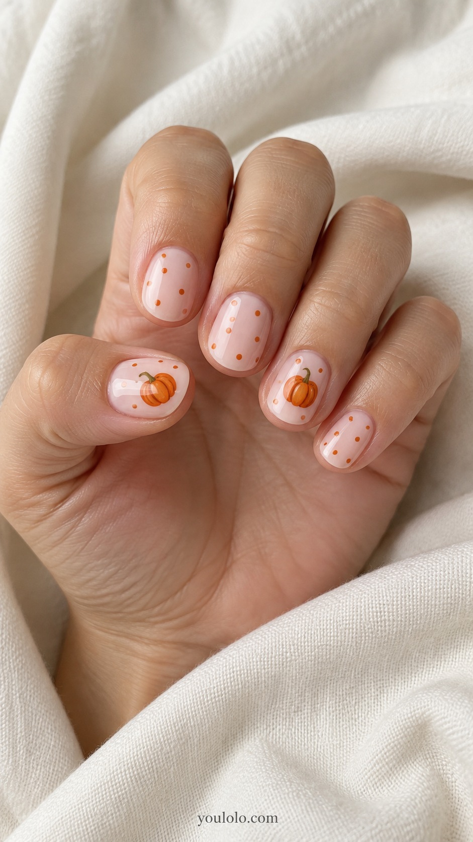 Short round nails pale pink base tiny orange pumpkins on ring and thumb other nails sparse orange polka dots