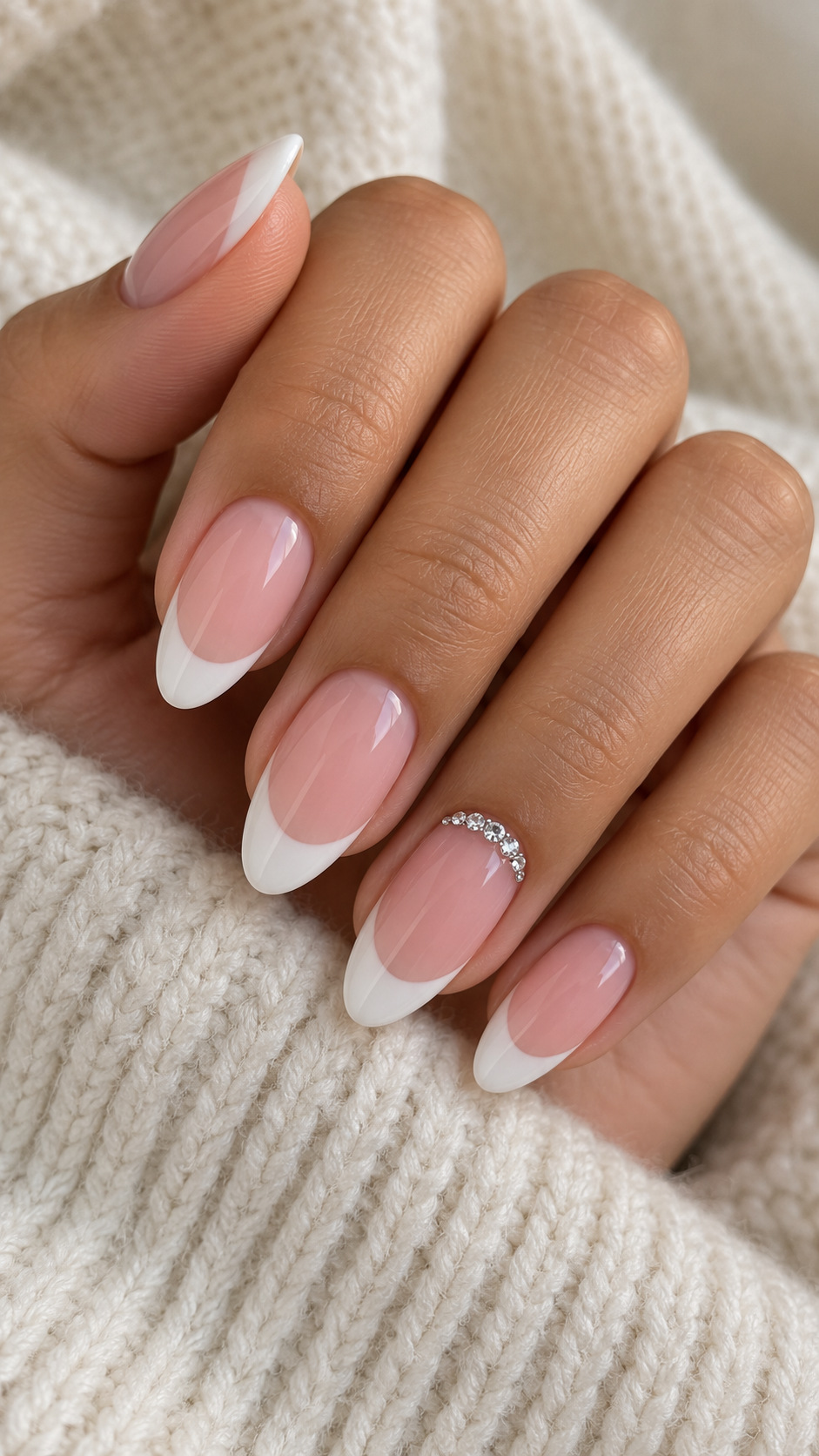 White French with a Crystal Cuticle Curve: Almond French nails with a small clear rhinestone arc on the ring finger on a naturally posed adult hand