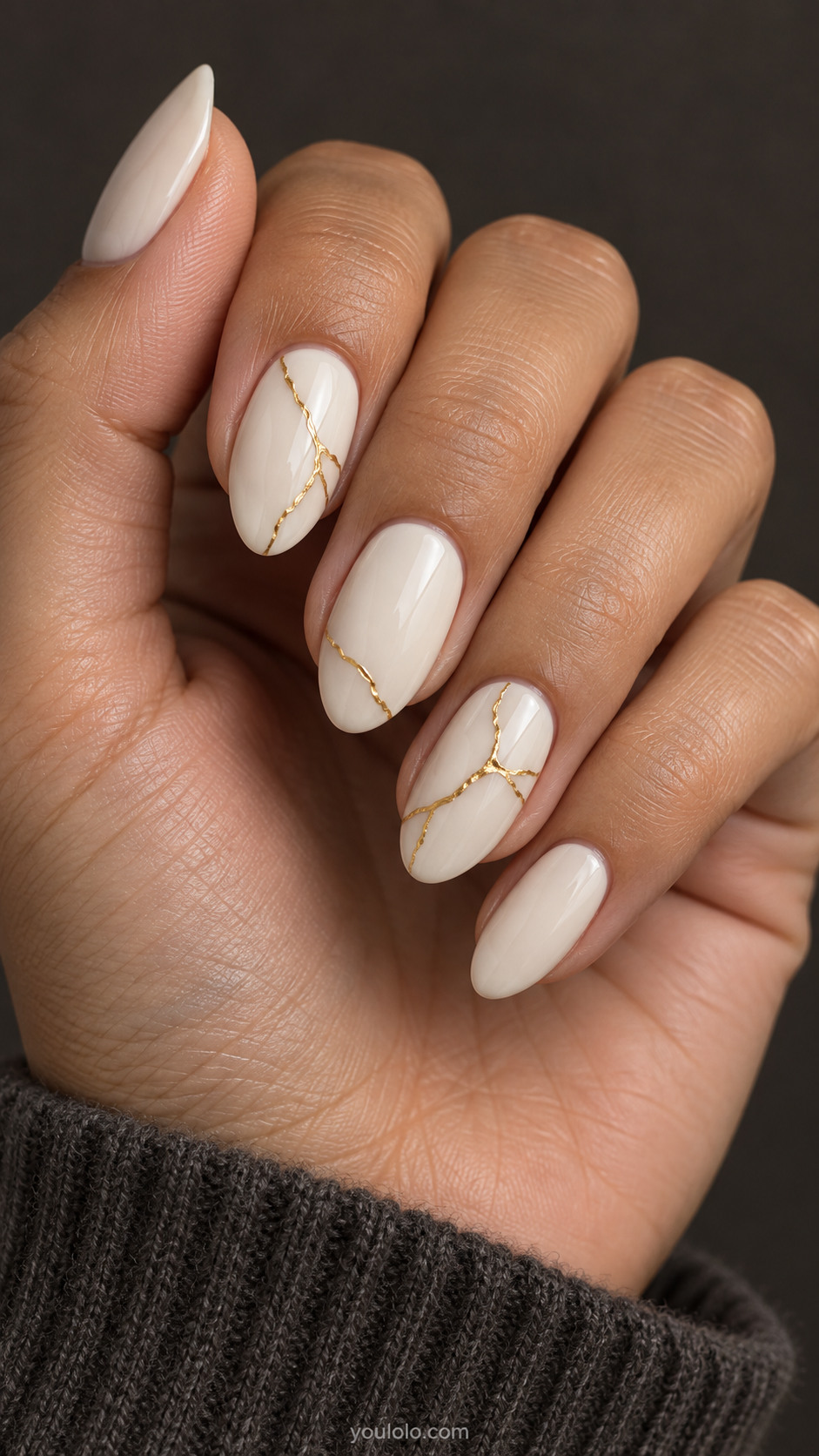 Medium almond nails, ivory base, fine branching gold seams on two nails with a small echo on a third