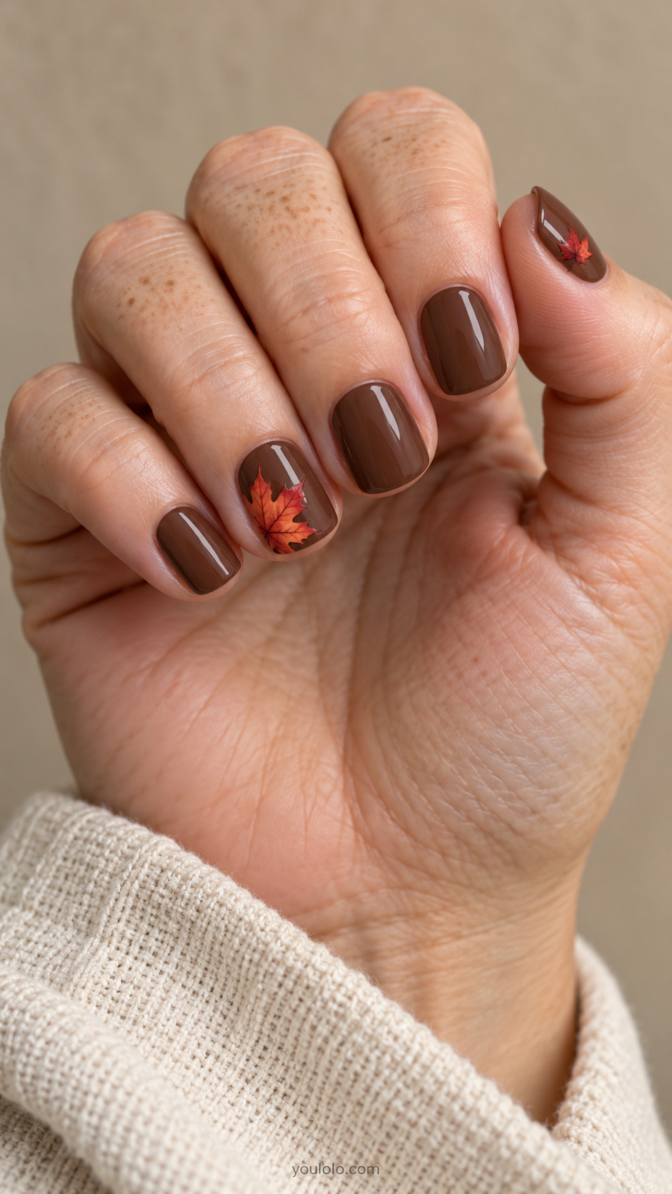 Short square nails with milk chocolate brown nails; one oversized flat painted vermilion maple leaf cropped deliberately into the outer corner of ring nail; thumbnail has a tiny matching leaf.