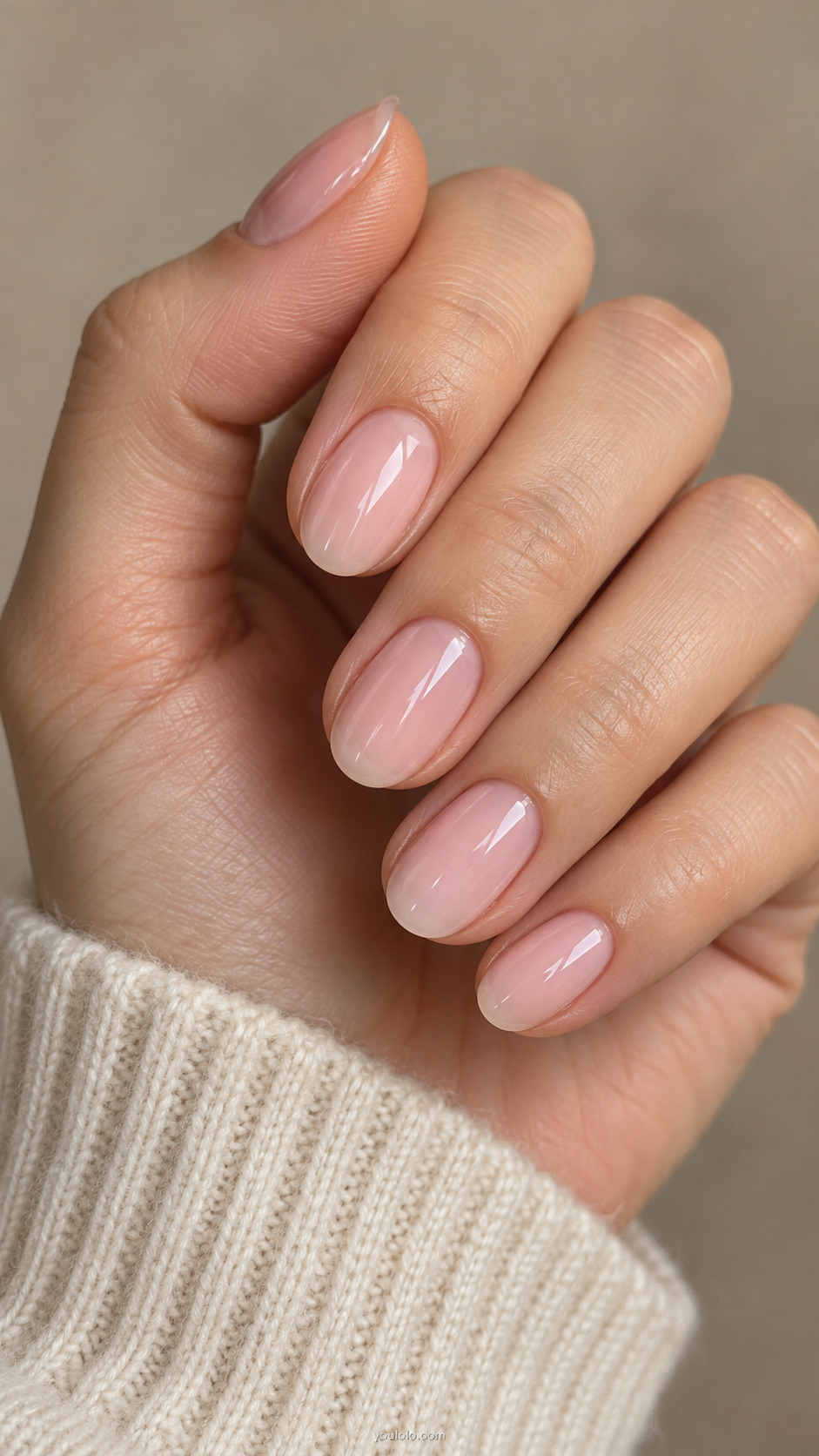 Short oval nails with translucent milky pink polish on a relaxed hand beside a cream knit cuff.