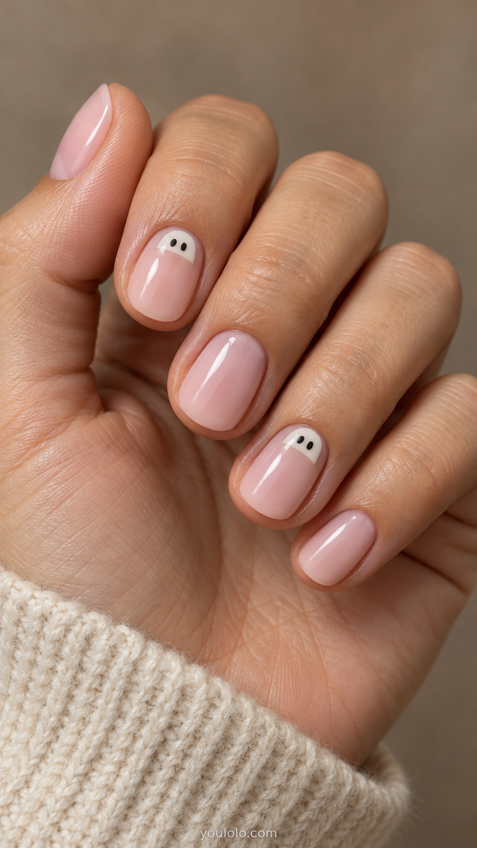 Short milky pink nails with ivory ghost faces peeking from two cuticles