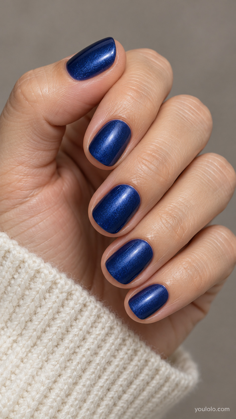 Short rounded sapphire blue nails with fine pearl sheen on a softly curled hand