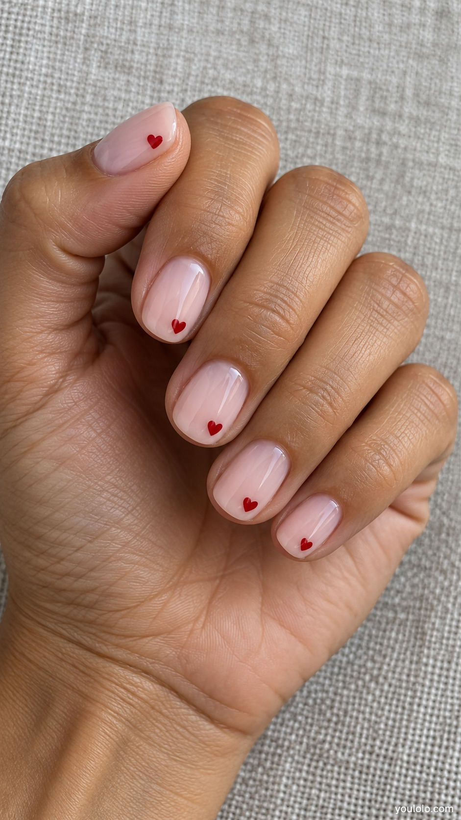 Short rounded milky pink nails with tiny red hearts near the tips