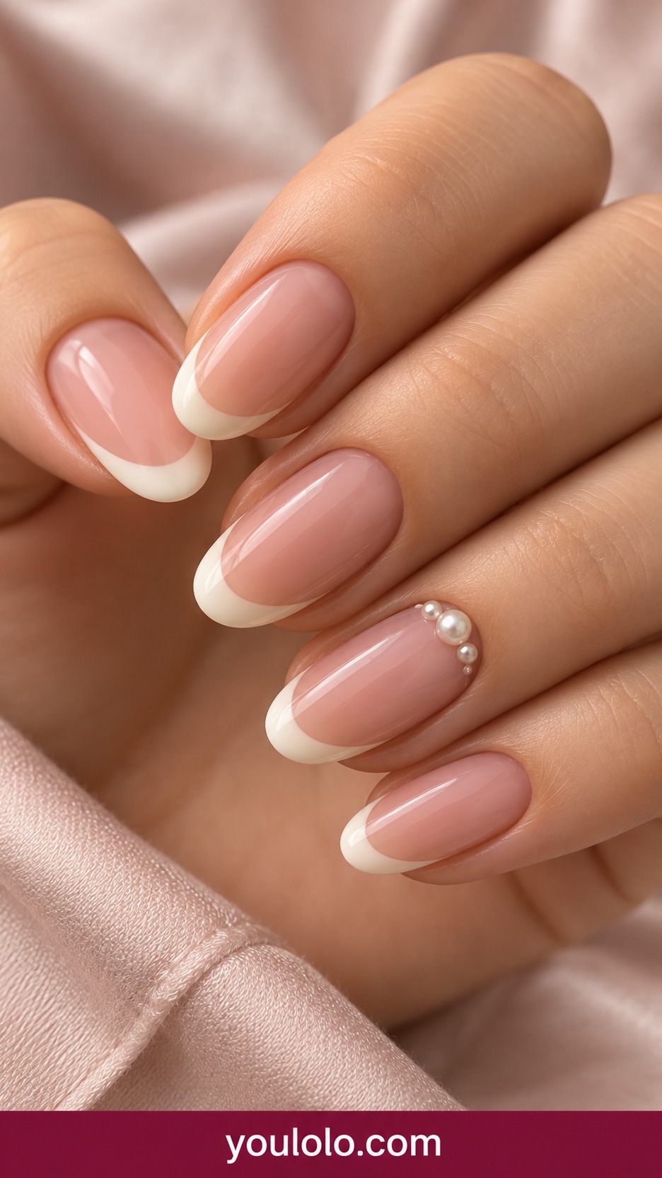 Medium oval translucent pink nails with ivory French tips and three tiny low profile pearl beads along one accent cuticle on a naturally curled young adult hand