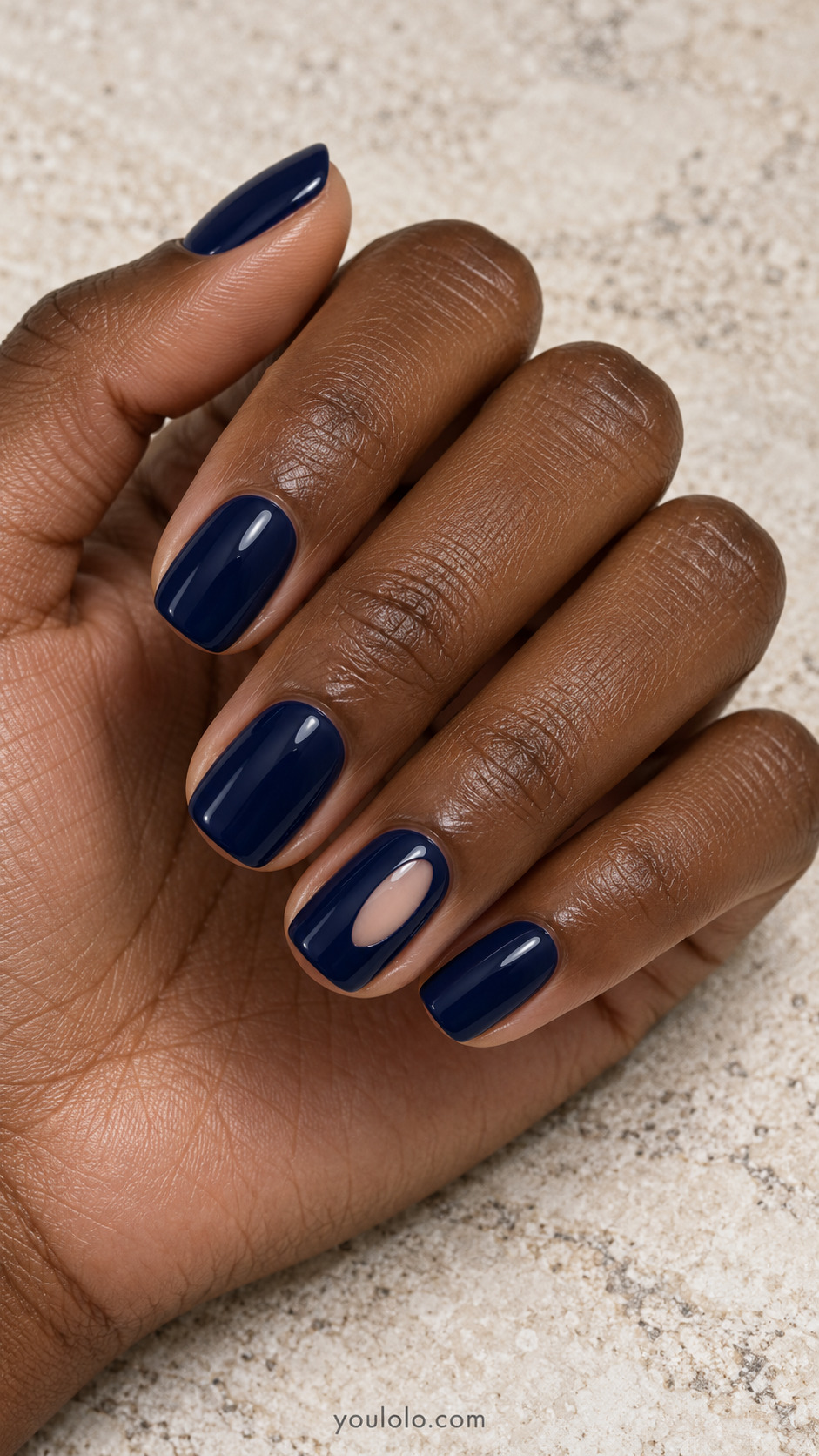 An Offset Nude Oval Window on a naturally posed hand, showing dark blue polish and detailed nail art