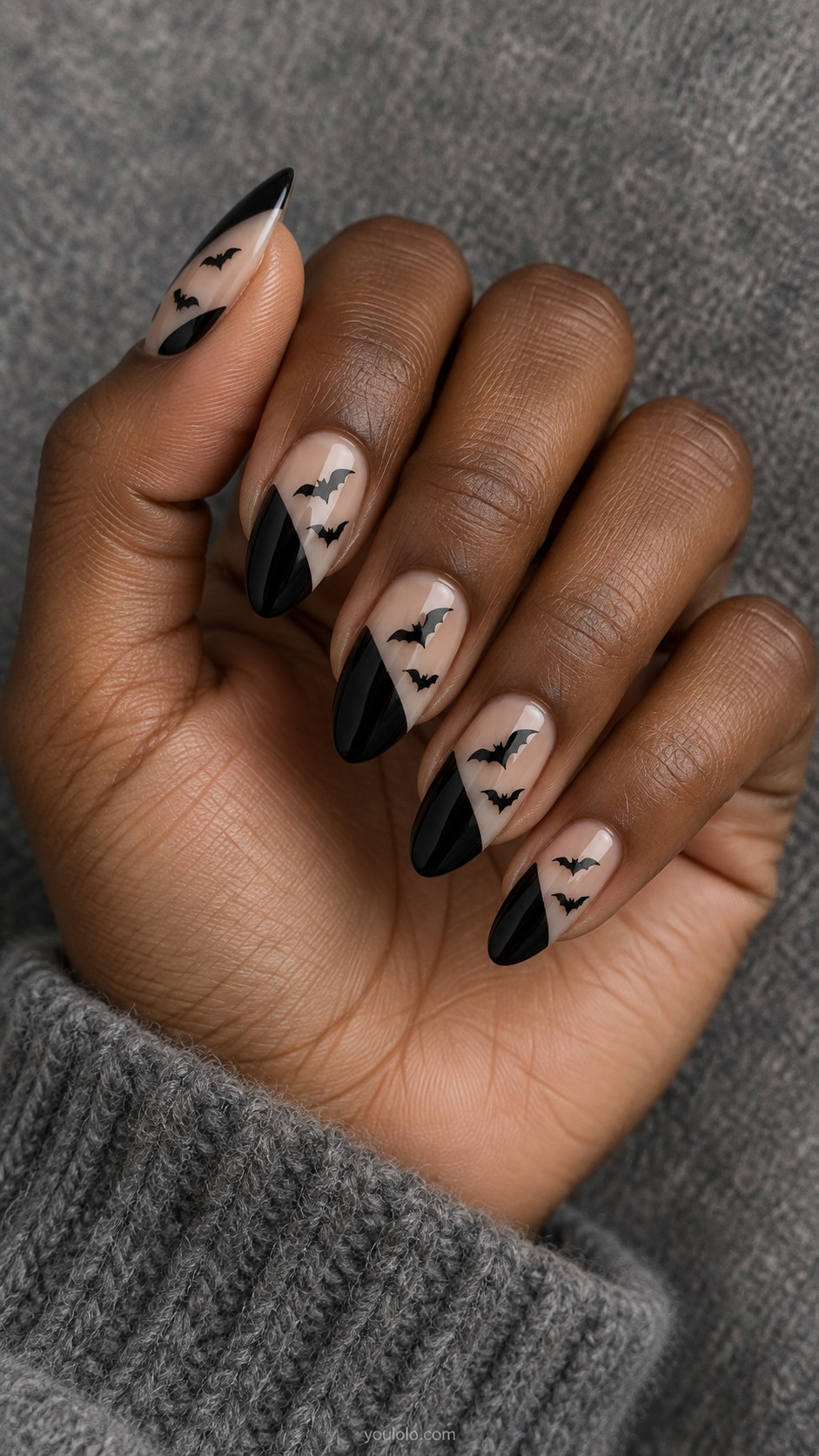 Medium almond nails translucent beige base with large opaque black diagonal panels; crisp little black bat silhouettes fly through clear diagonal channels