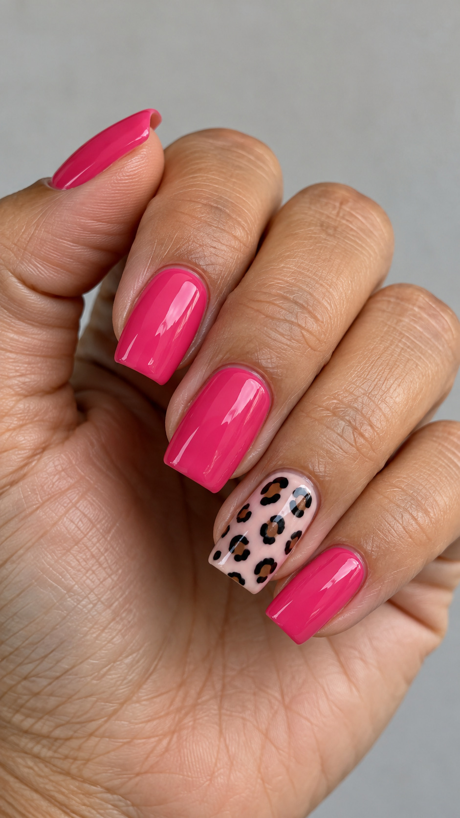 Hot Pink with a Leopard Accent: Hot pink square nails with leopard spots on a pale pink ring nail on a naturally posed adult hand