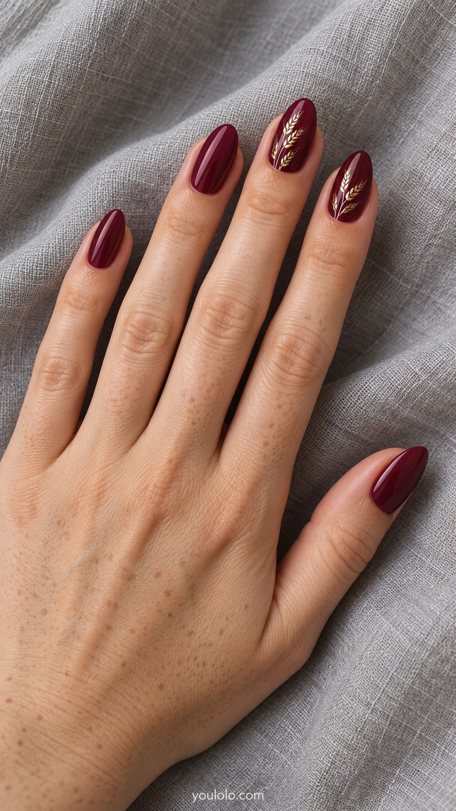 Medium almond nails burgundy cream with delicate gold painted wheat sprigs on ring and middle