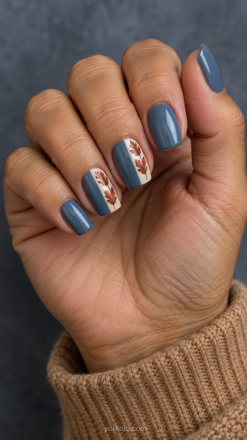 Medium squoval nails with opaque dusty denim blue nails with a thin vertical ivory panel along one side of middle and ring; tiny flat rust oak leaves arranged vertically in panels.