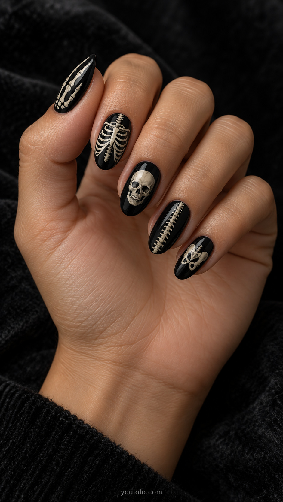 Medium oval glossy black nails each with a different minimalist ivory skeleton segment, slender ribcage, finger bones, tiny skull, spine, very fine handpainted