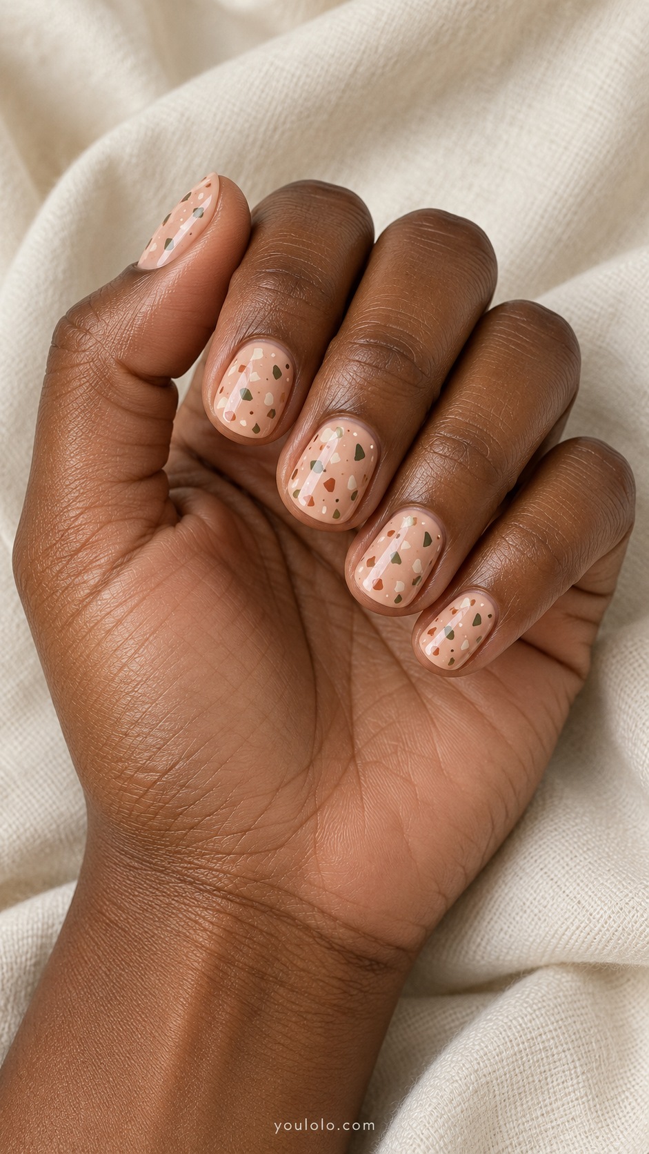 Short round nails muted peach base irregular tiny olive cream and rust flat terrazzo flecks