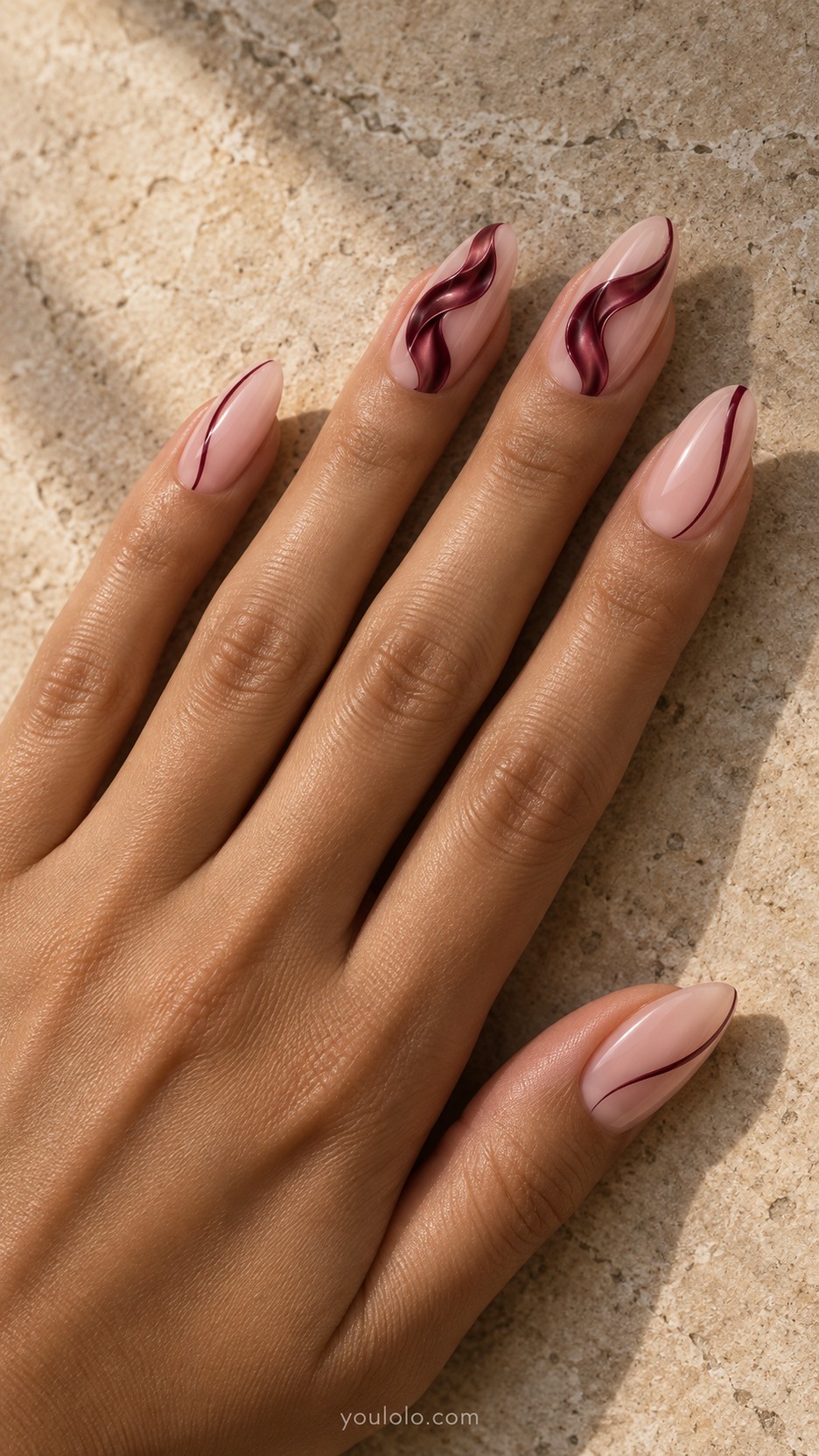 Burgundy Ribbon Sculpture — Medium almond nails, milky nude pink base, burgundy low-relief flowing folded ribbon down two accent nails with smooth edges and apparent folded satin thickness, fine burgundy side strokes other nails
