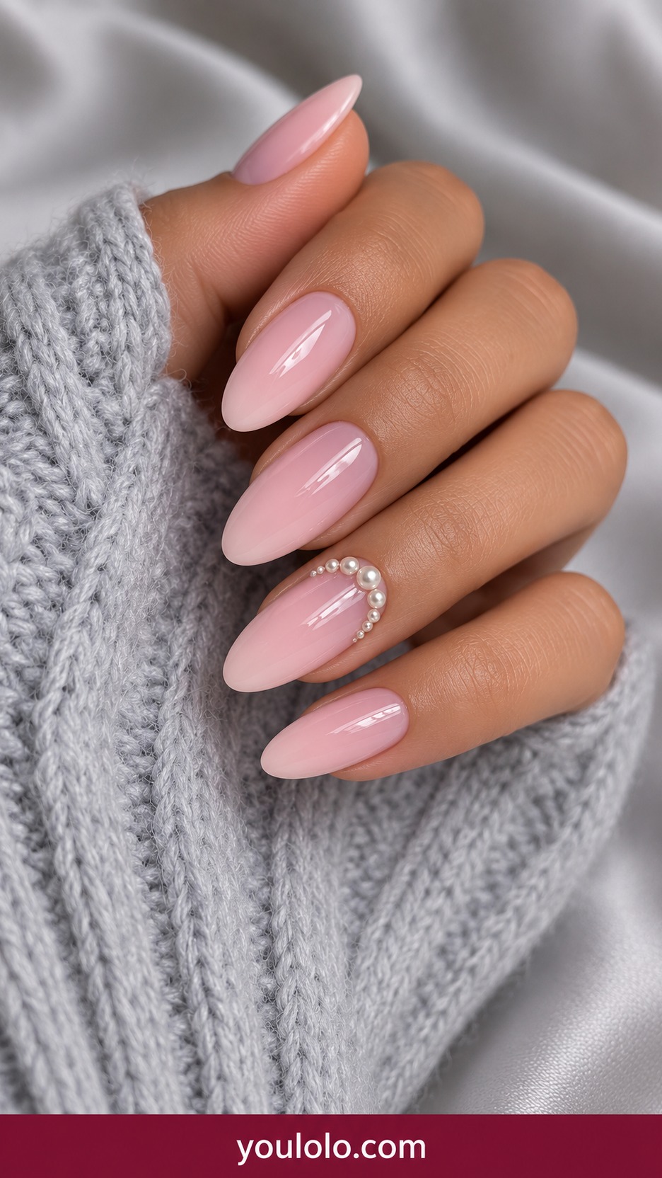 Medium almond blush pink nails with small low profile ivory pearls forming an arch on one accent on a naturally curled young adult hand