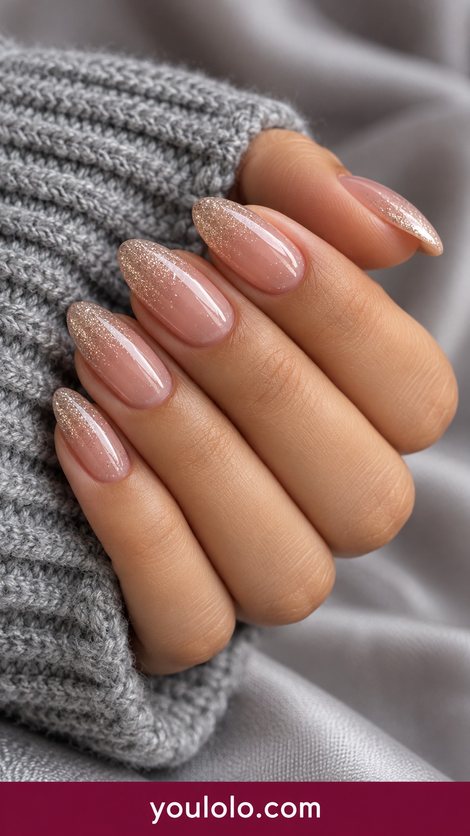 Medium almond sheer beige pink nails with very fine champagne sparkle fading from tips into transparent base on a naturally curled young adult hand