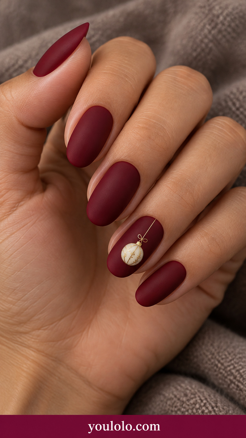 medium oval ruby red cream nails with one miniature round ivory bauble outlined gold suspended from thin gold line on ring nail on a naturally relaxed adult hand