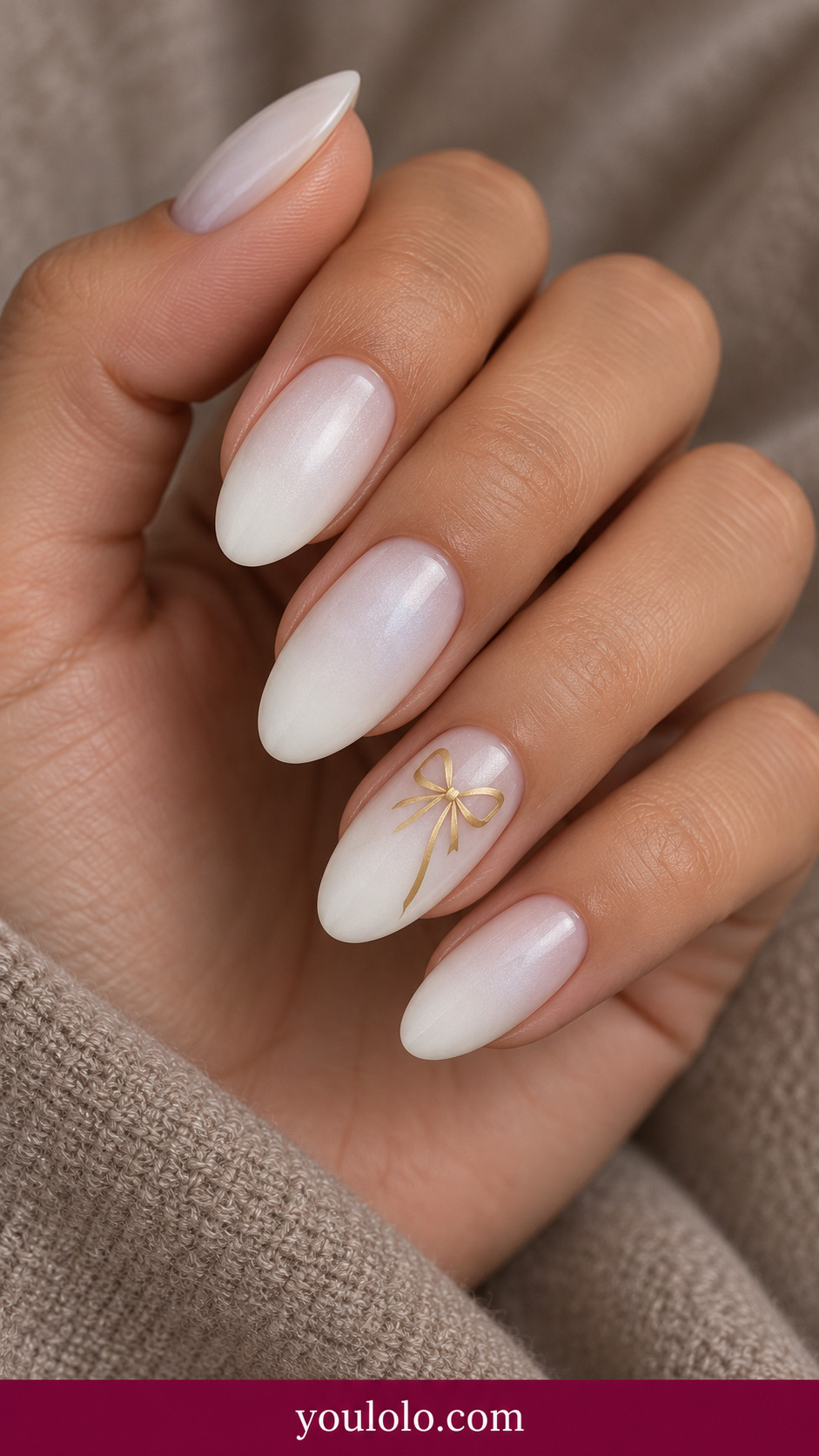medium oval soft white pearl nails one tiny flat painted champagne gold bow with long fine tails on ring nail on a naturally relaxed adult hand