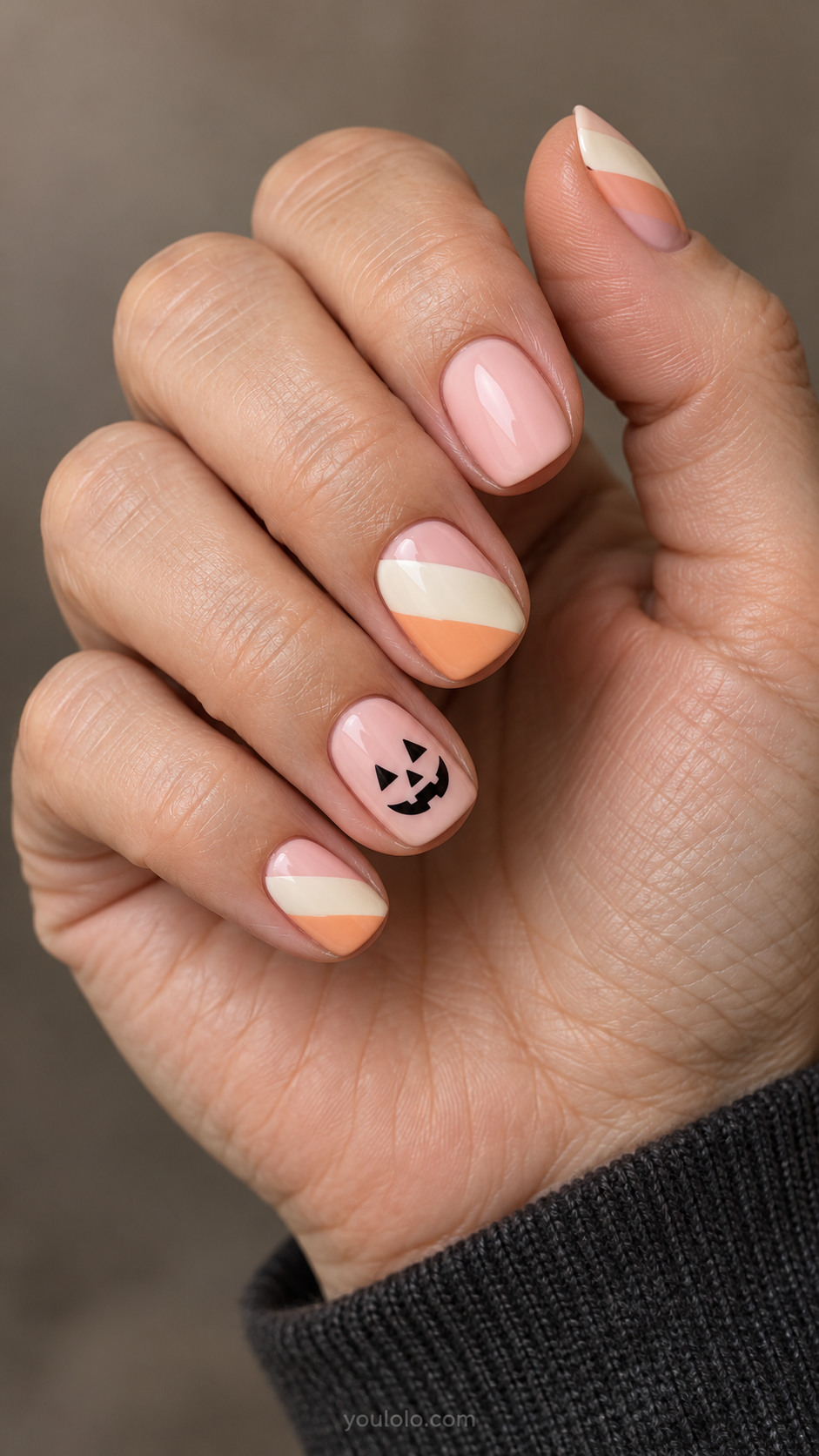 Short pink nails with cream and peach diagonal blocks and a pumpkin face