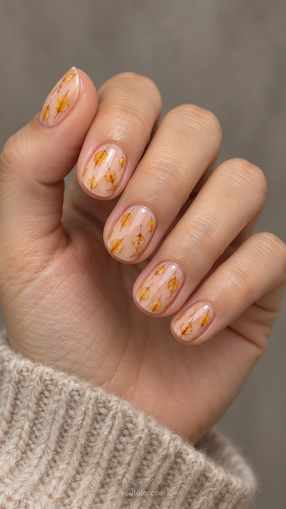Short round nails with sheer peach nails with five or six tiny diamond-shaped yellow birch leaves scattered across each nail, fine brown stems, generous clear space.