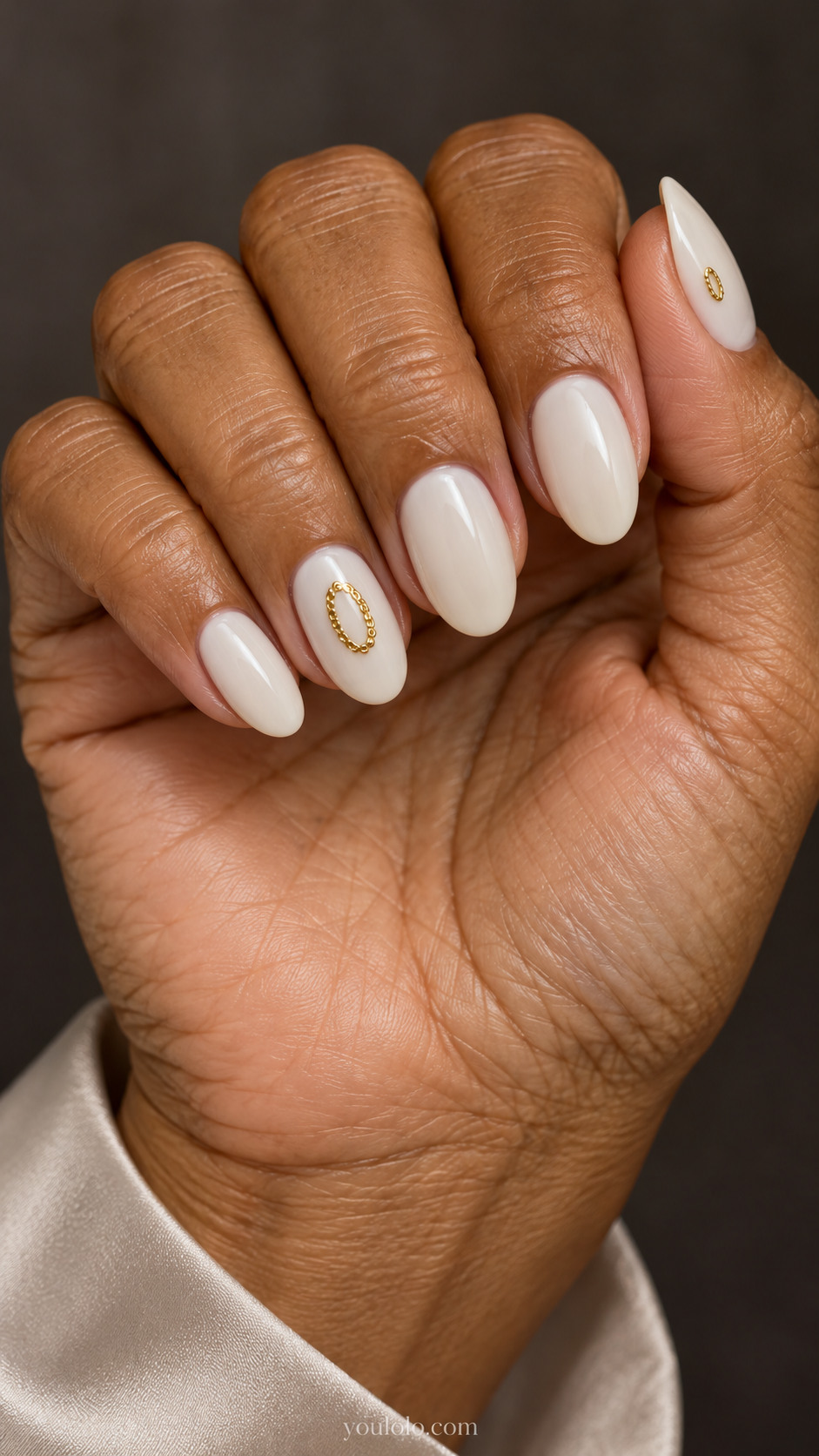 Medium oval ivory nails with a small low-profile oval chain medallion on the ring nail and a smaller one on the thumb