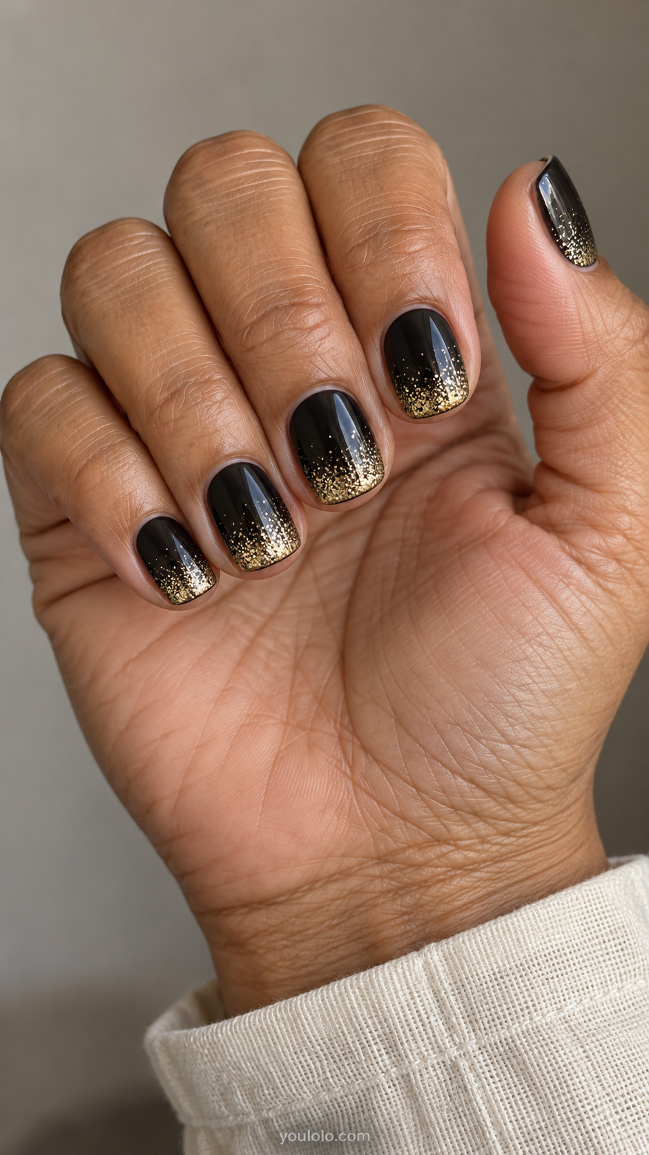 Short glossy black nails with fine gold glitter concentrated at the tips