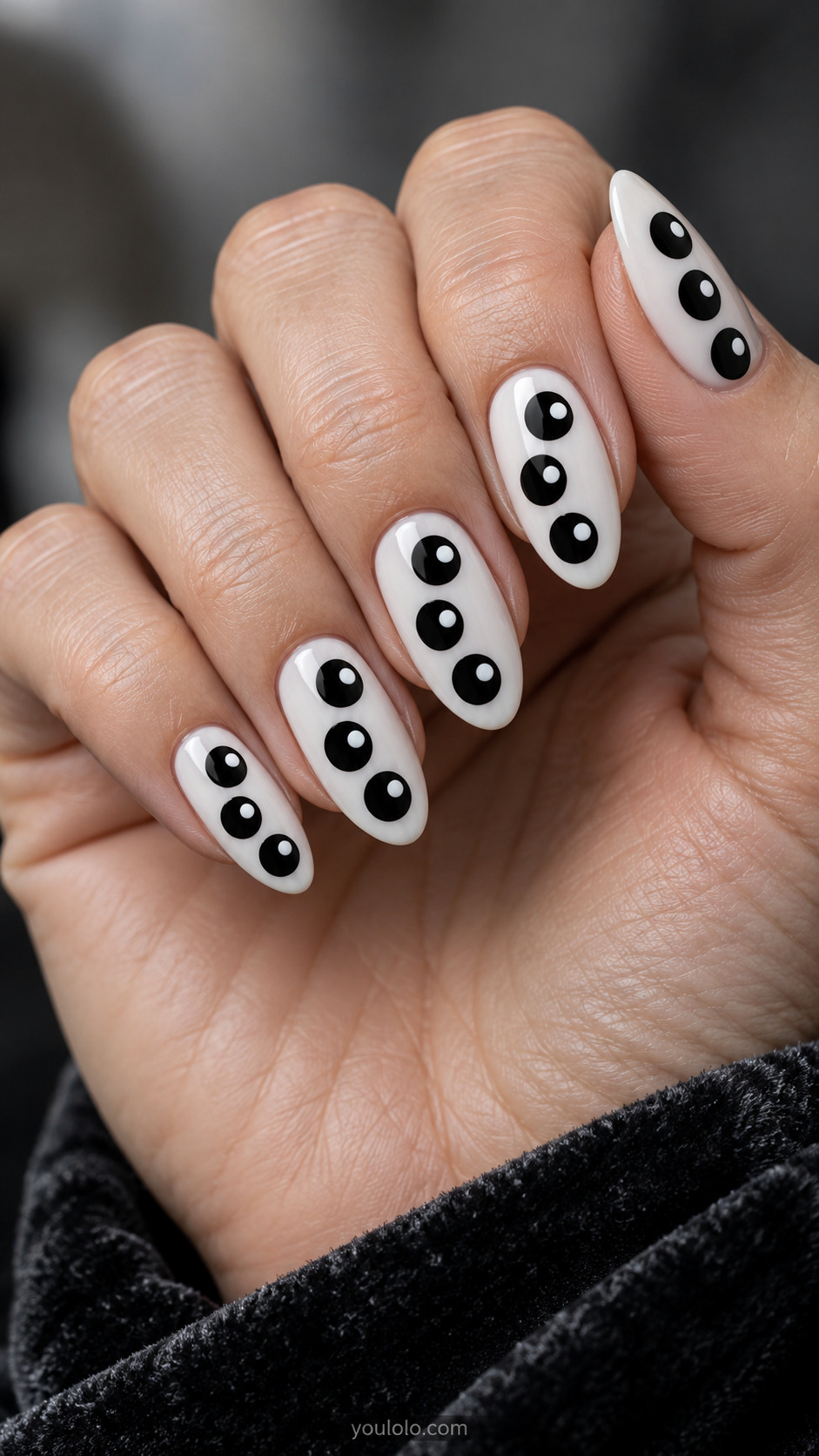 Medium almond milky white nails with three large black circles per nail each containing small white dot offset toward one side, flat paint