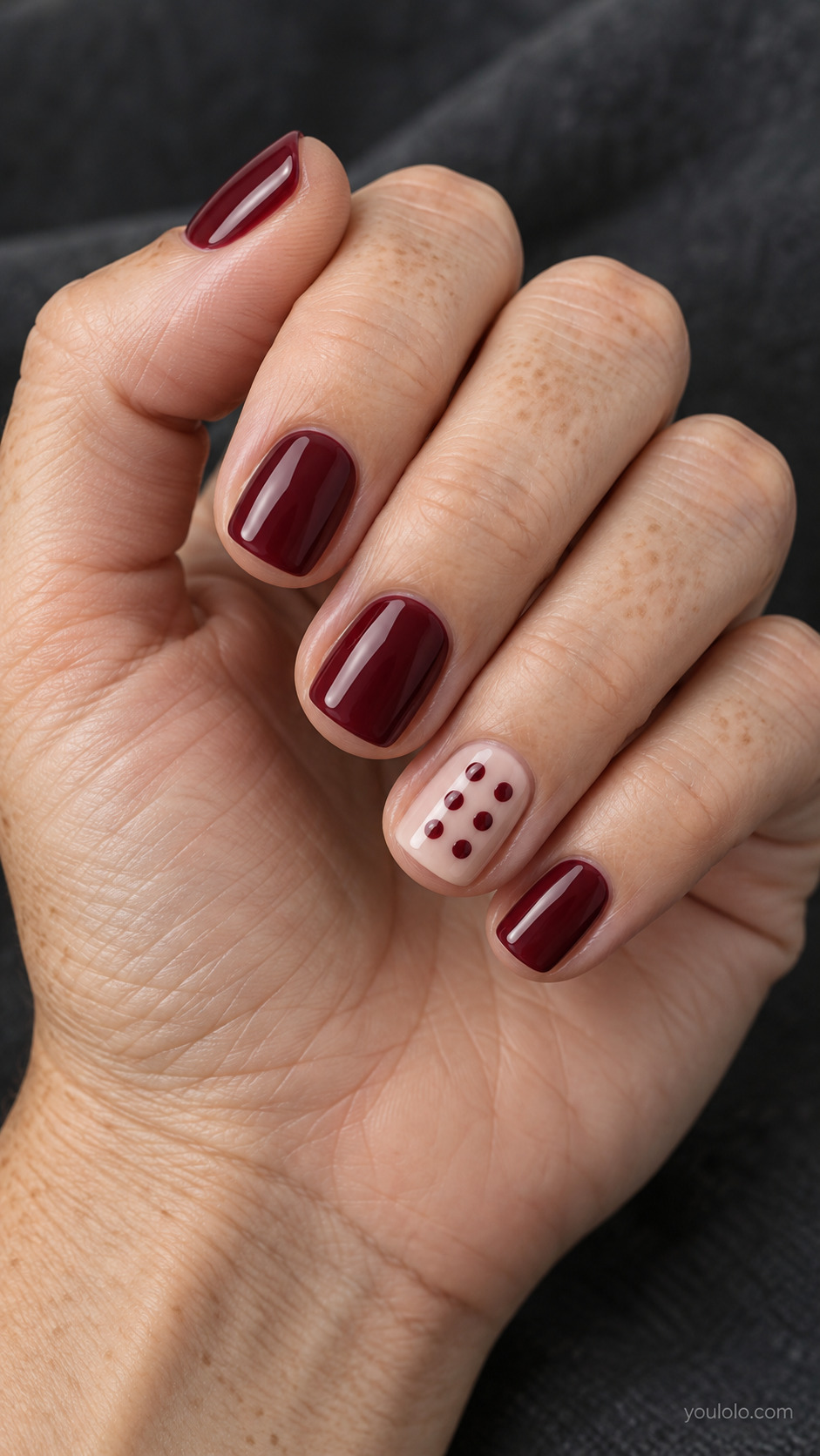 Short squoval nails: four solid glossy merlot nails, ring finger pale neutral with tidy burgundy dots.
