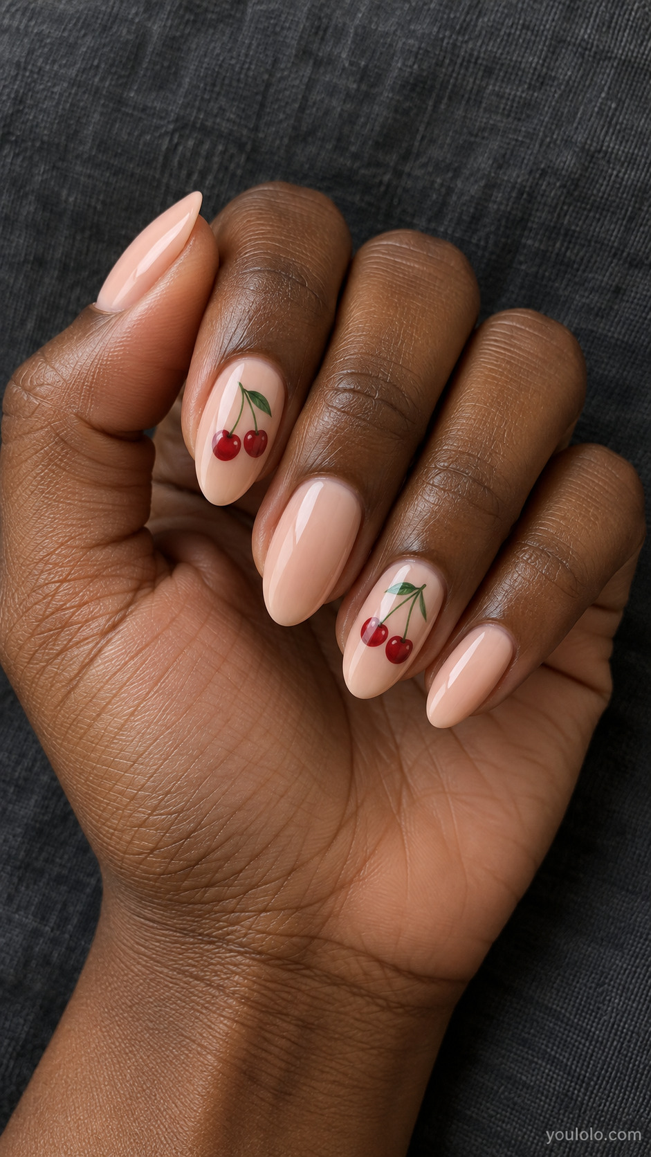 Peach almond nails with small red cherry pairs and green stems on two nails