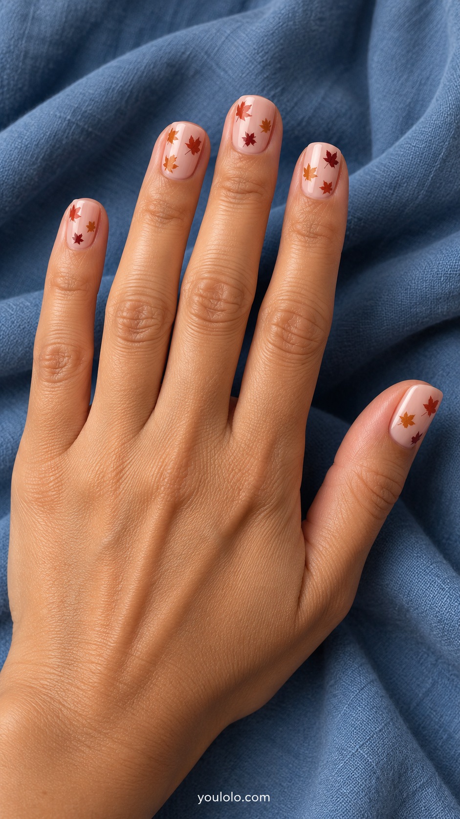 Short squoval nails pale peach base tiny flat rust ochre and burgundy maple leaf silhouettes scattered lightly