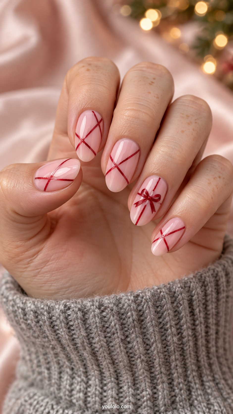 Medium oval blush pink nails slim red crisscross ribbon lines and one small flat red bow on ring nail