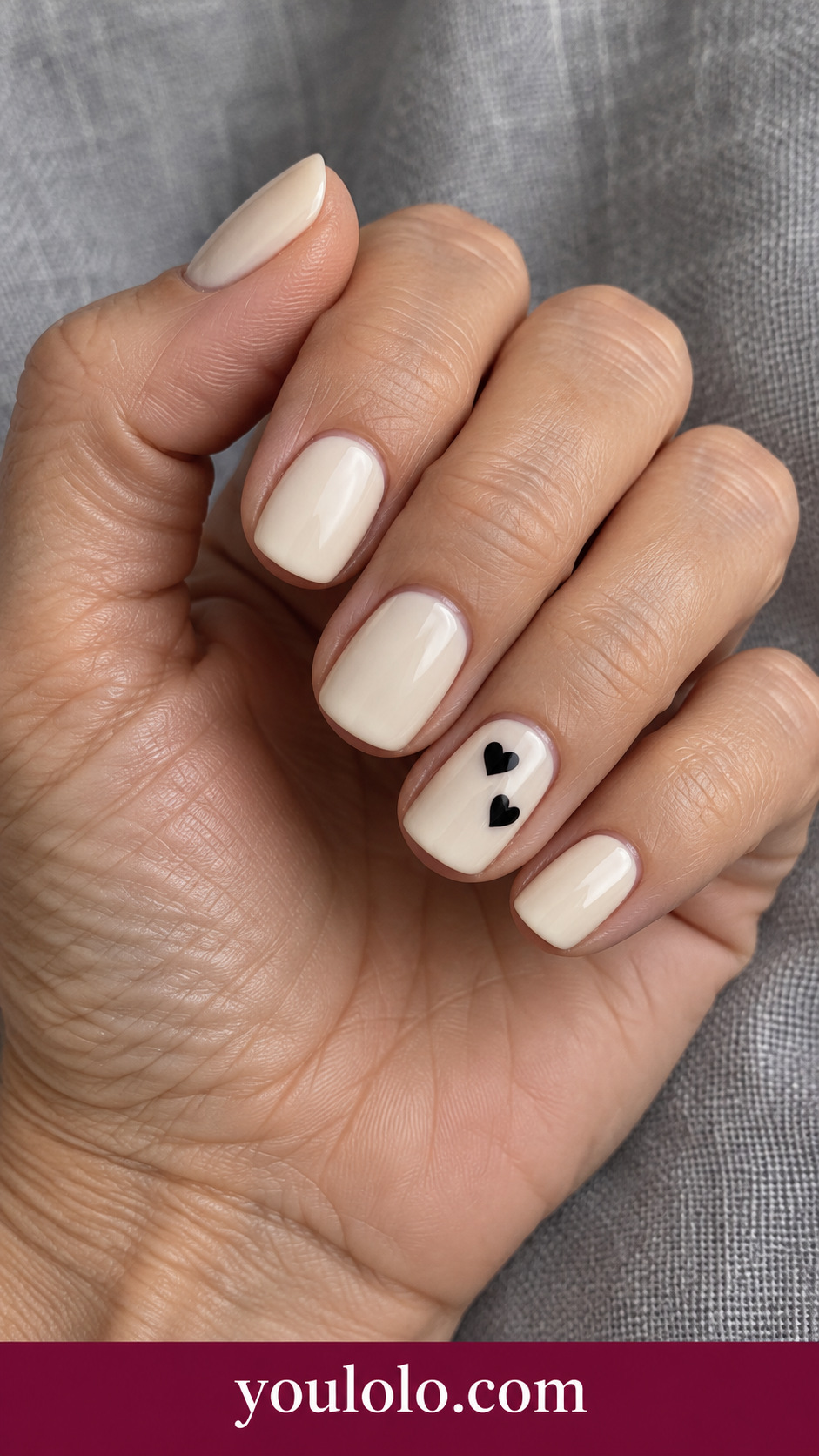Black Heart Pair: short squoval creamy ivory nails two small black hearts diagonally on one accent nail on a naturally posed adult hand