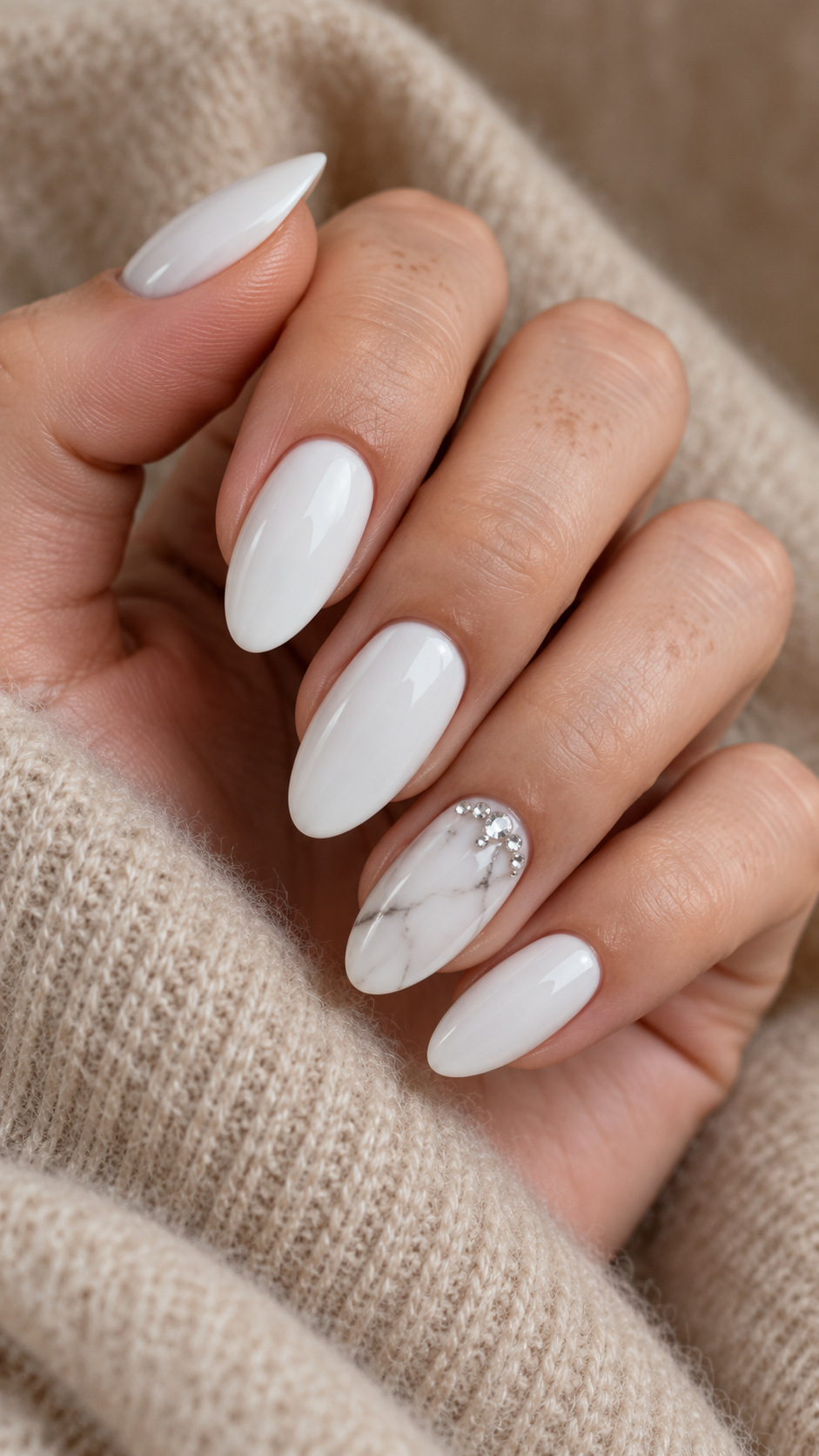 White Marble with Crystal Detail: White almond nails with gray marble and a crystal cluster on the ring nail on a naturally posed adult hand