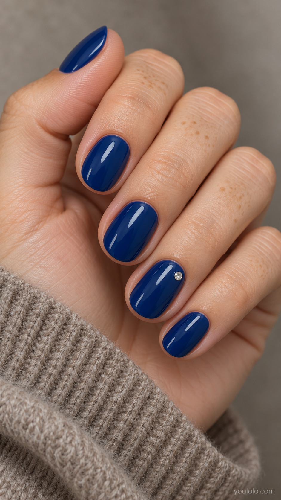 A Single Crystal on Sapphire on a softly gathered feminine hand with detailed sapphire blue manicure