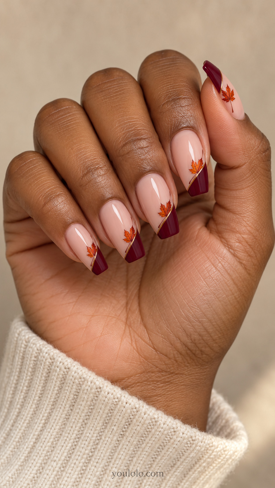 Medium coffin nails with nude nails with diagonal burgundy French corners; one small burnt orange five-point maple leaf positioned along each diagonal border, flat art.