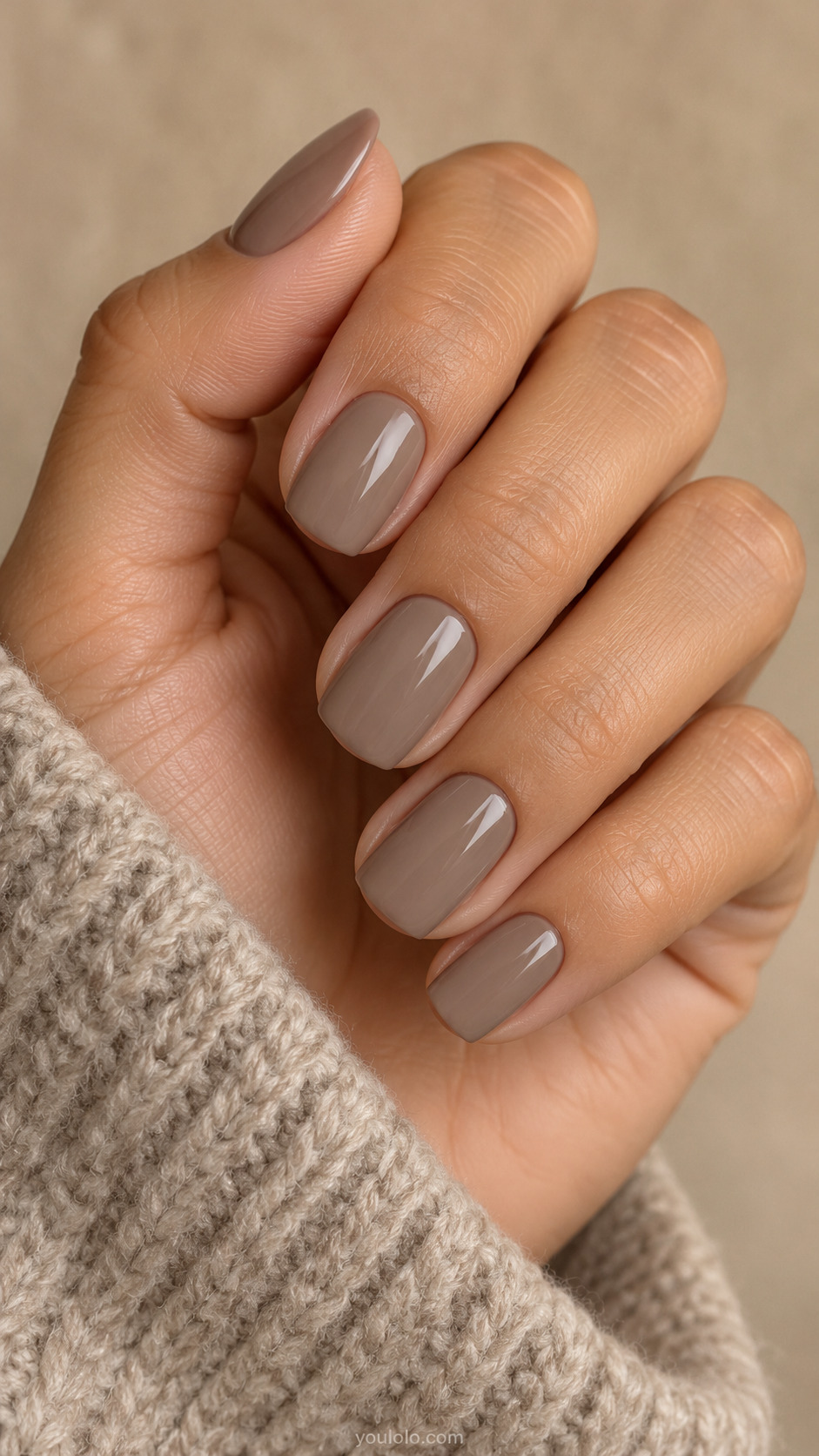 Short squoval nails with glossy mushroom taupe polish beside a stone-colored knit cuff.